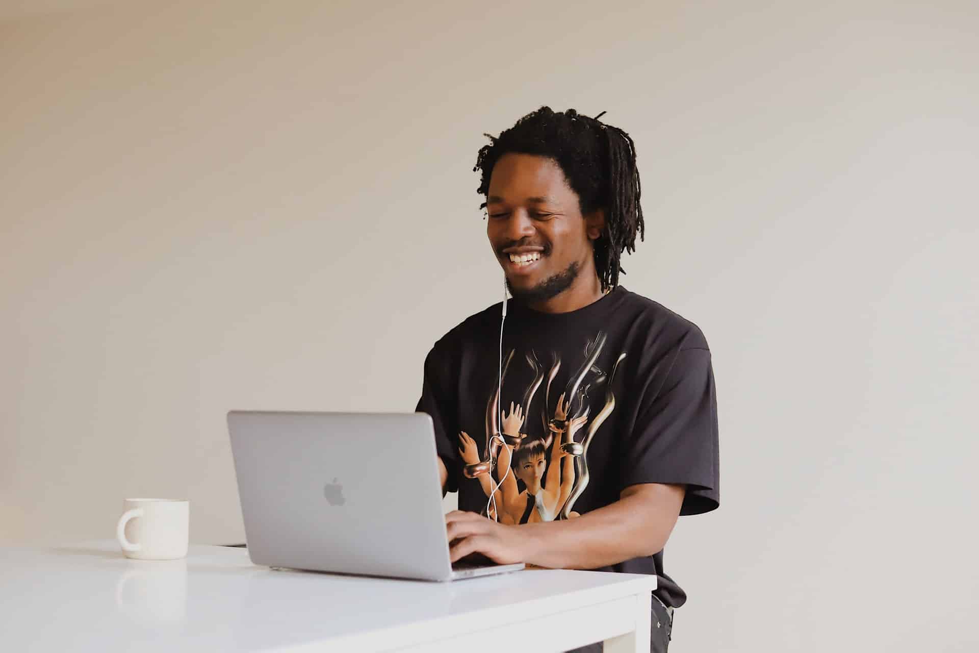 Homem com cabelos em dreadlocks sorri ao olhar para o laptop.