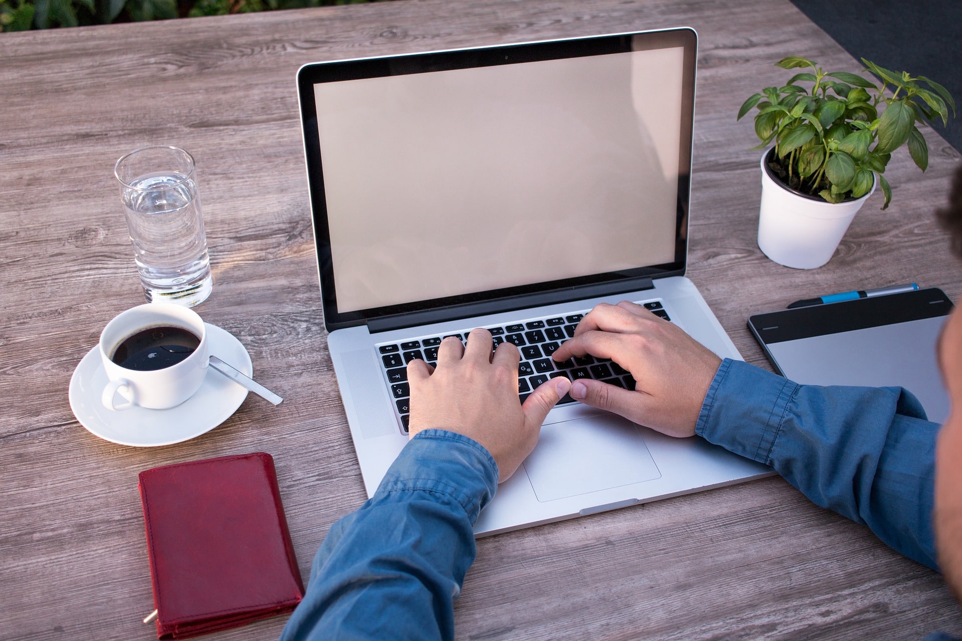 Homem trabalhando em um notebook com uma xícara de café e um copo com água do lado.