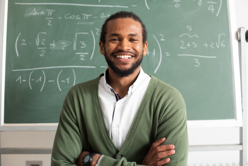 Professor sorrindo na frente de um quadro negro