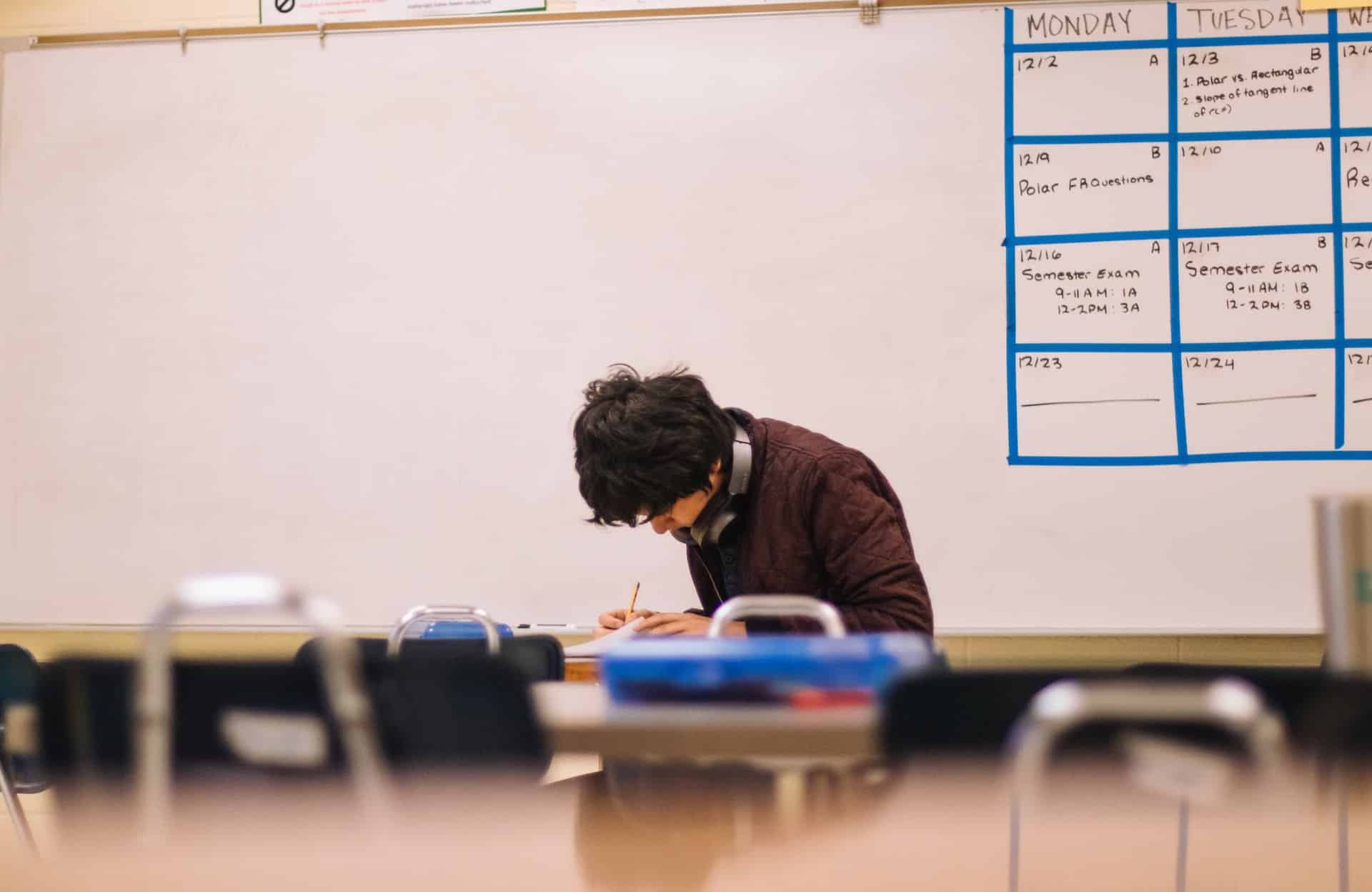 Adolescente estudando em uma sala de aula com um quadro branco ao fundo.