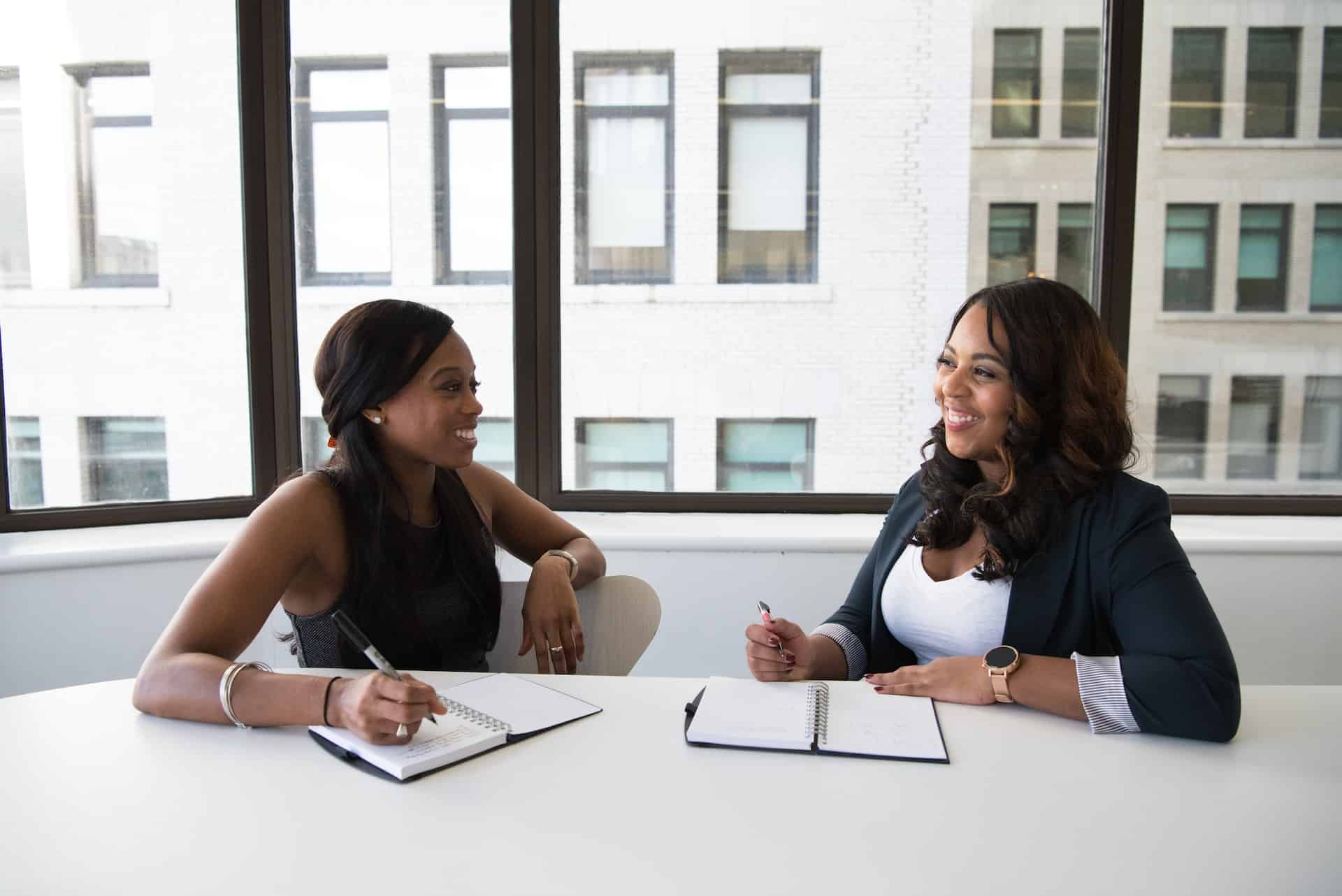 duas mulheres negras conversando em uma mesa de forma formal