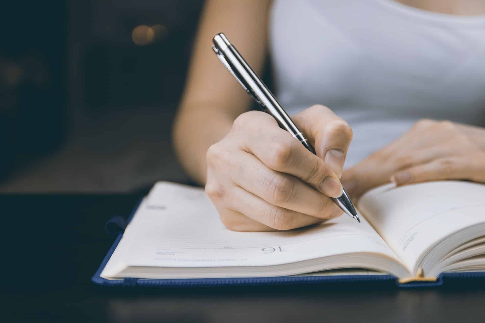 Mão com caneta escrevendo no caderno