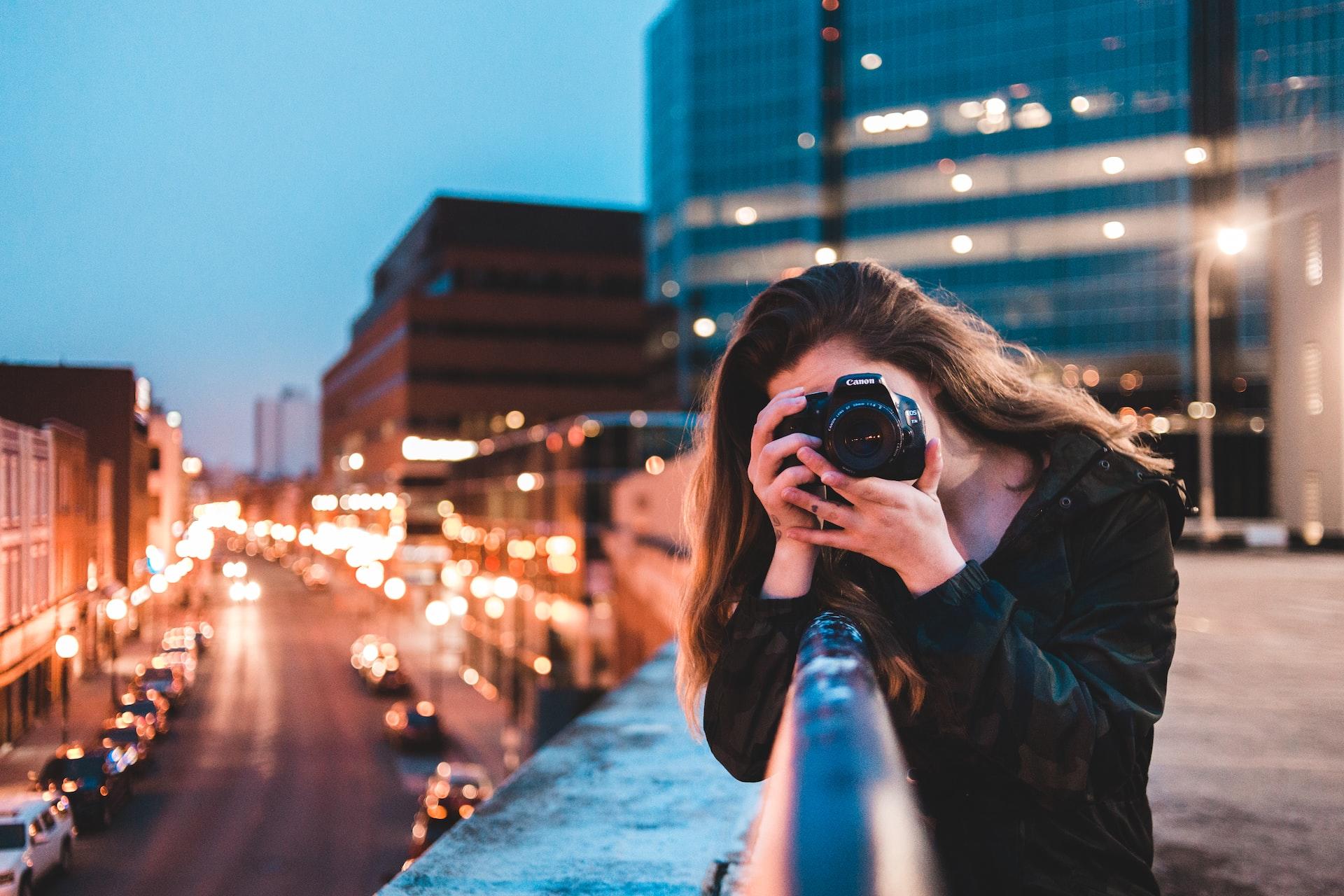 Mulher tirando uma fotografia em uma cidade a noite.