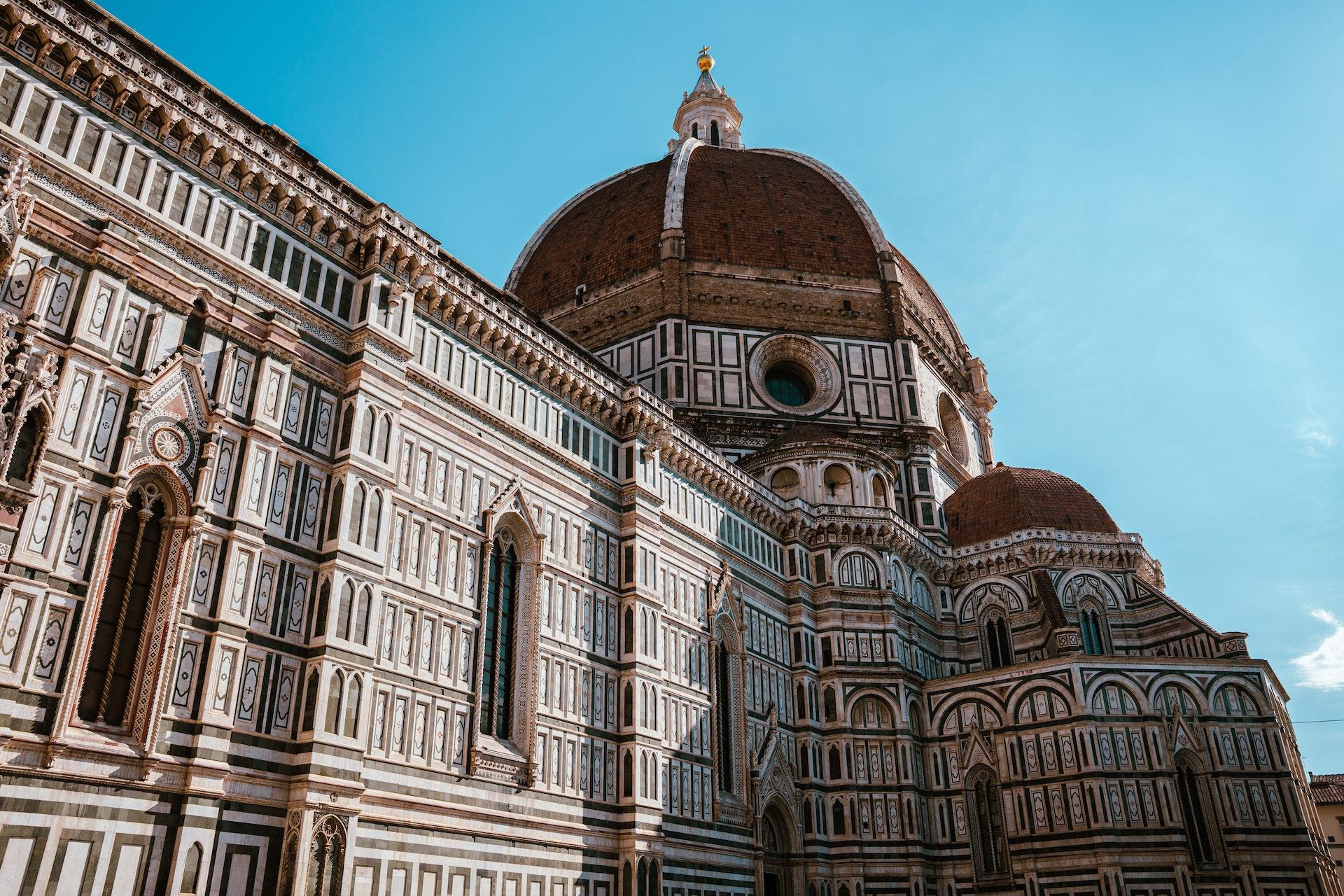 Foto de perto da Catedral de Santa Maria del Fiore, em tons de marrom e bege, à frente de um céu azul. 