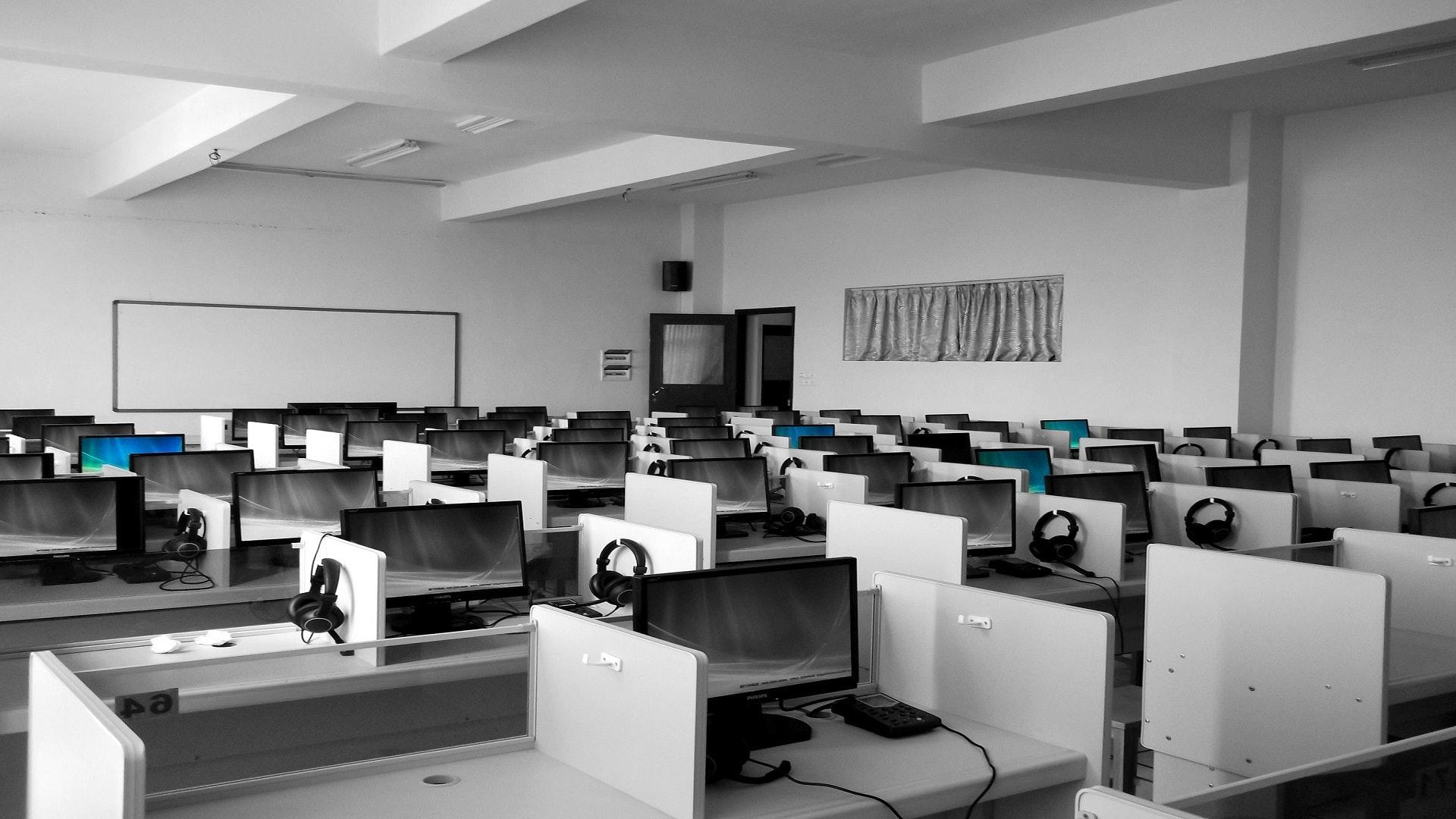 Laboratório de computadores. A foto está em preto e branco e mostra uma sala com muitos computadores. Sugere sala de aula de informática ou escritório. 