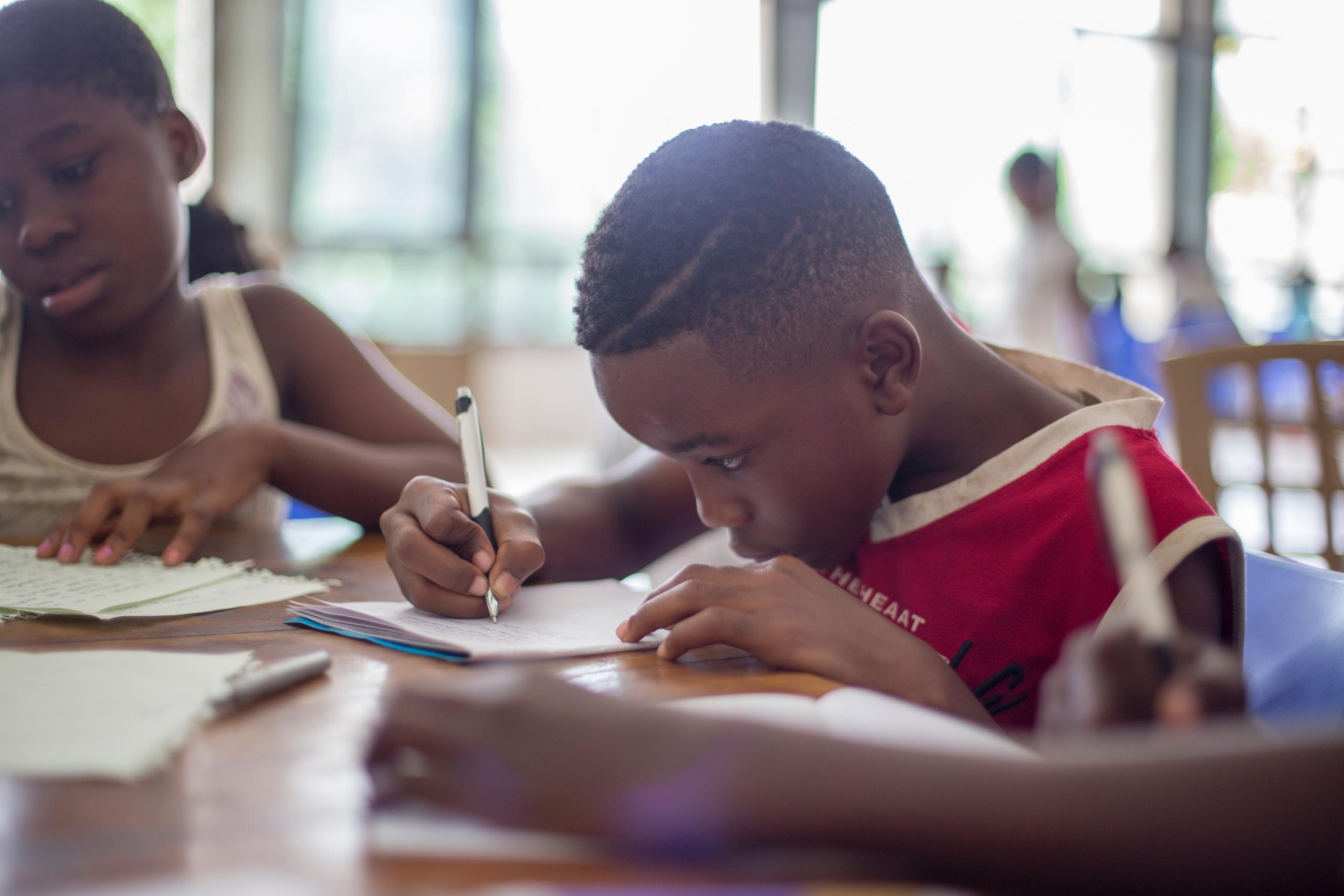 Menino negro escrevendo no caderno na volta às aulas