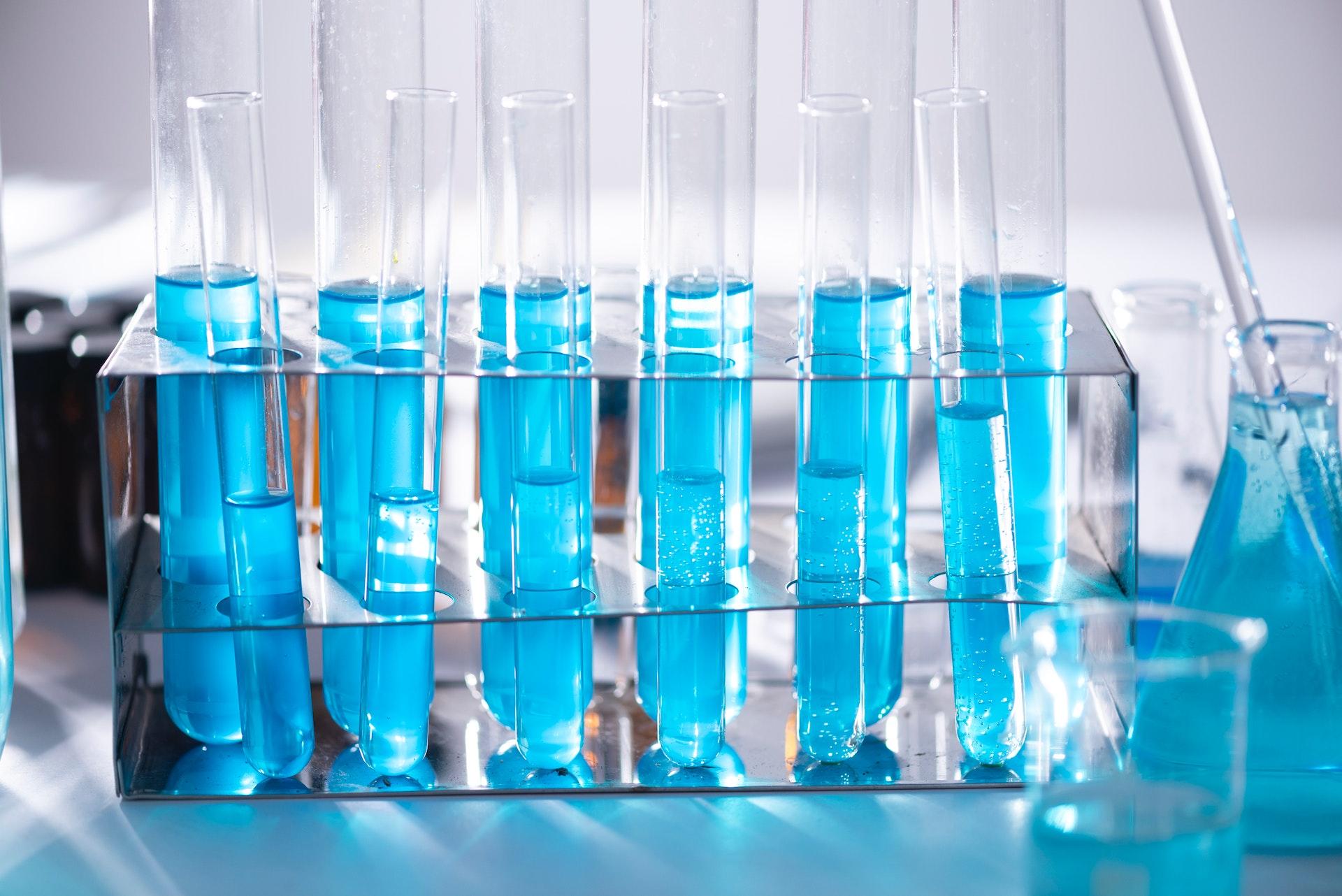 A foto mostra uma sequência de 6 tubos de ensaio com líquido azul em um suporte em laboratório.