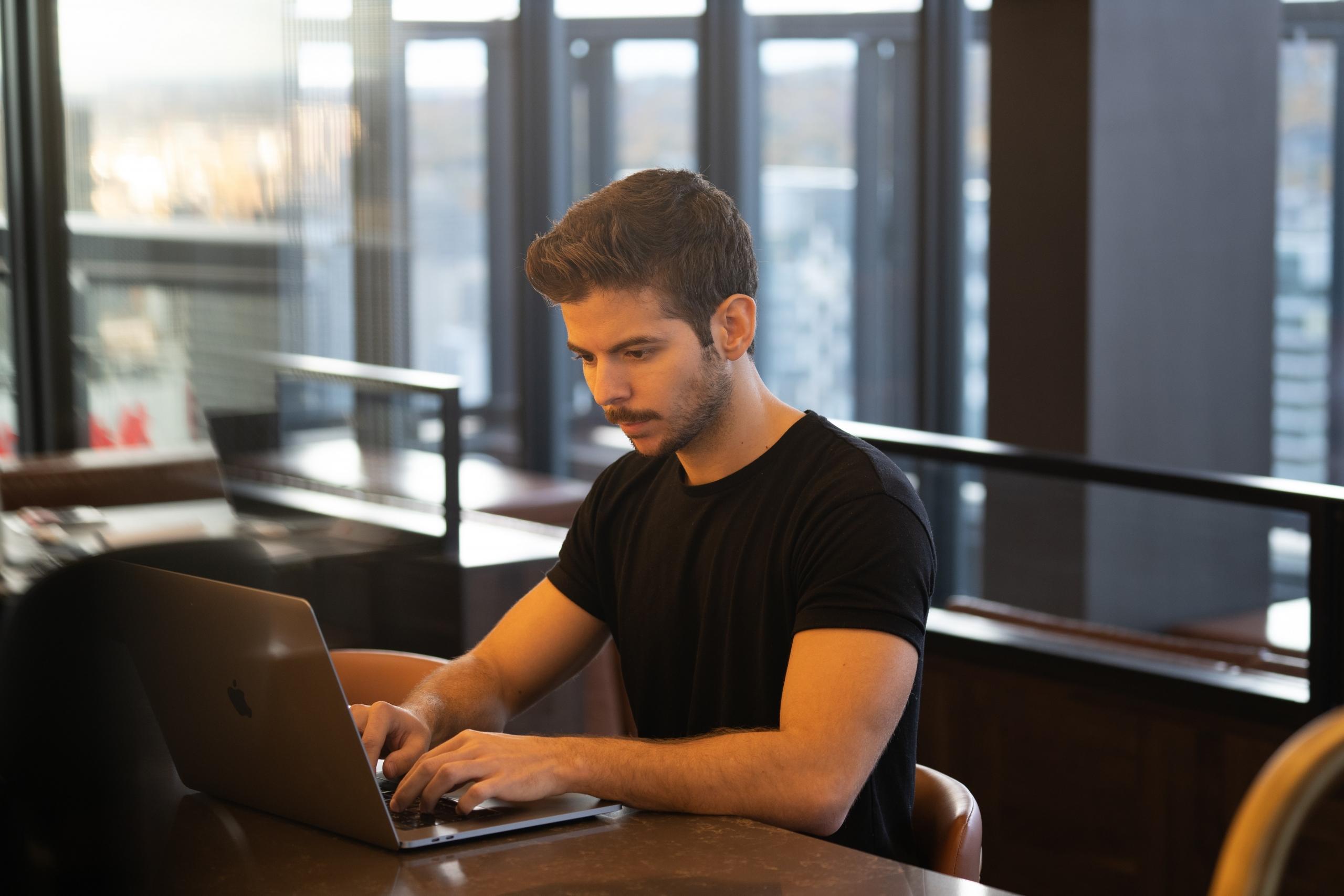 Homem de frente a um computador usando camiseta preta e cabelo curto