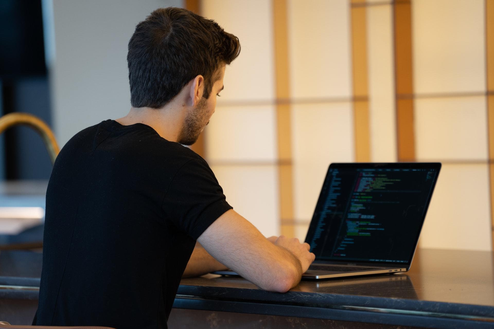 Rapaz sentado diante de um computador com linguagem de programação na tela.