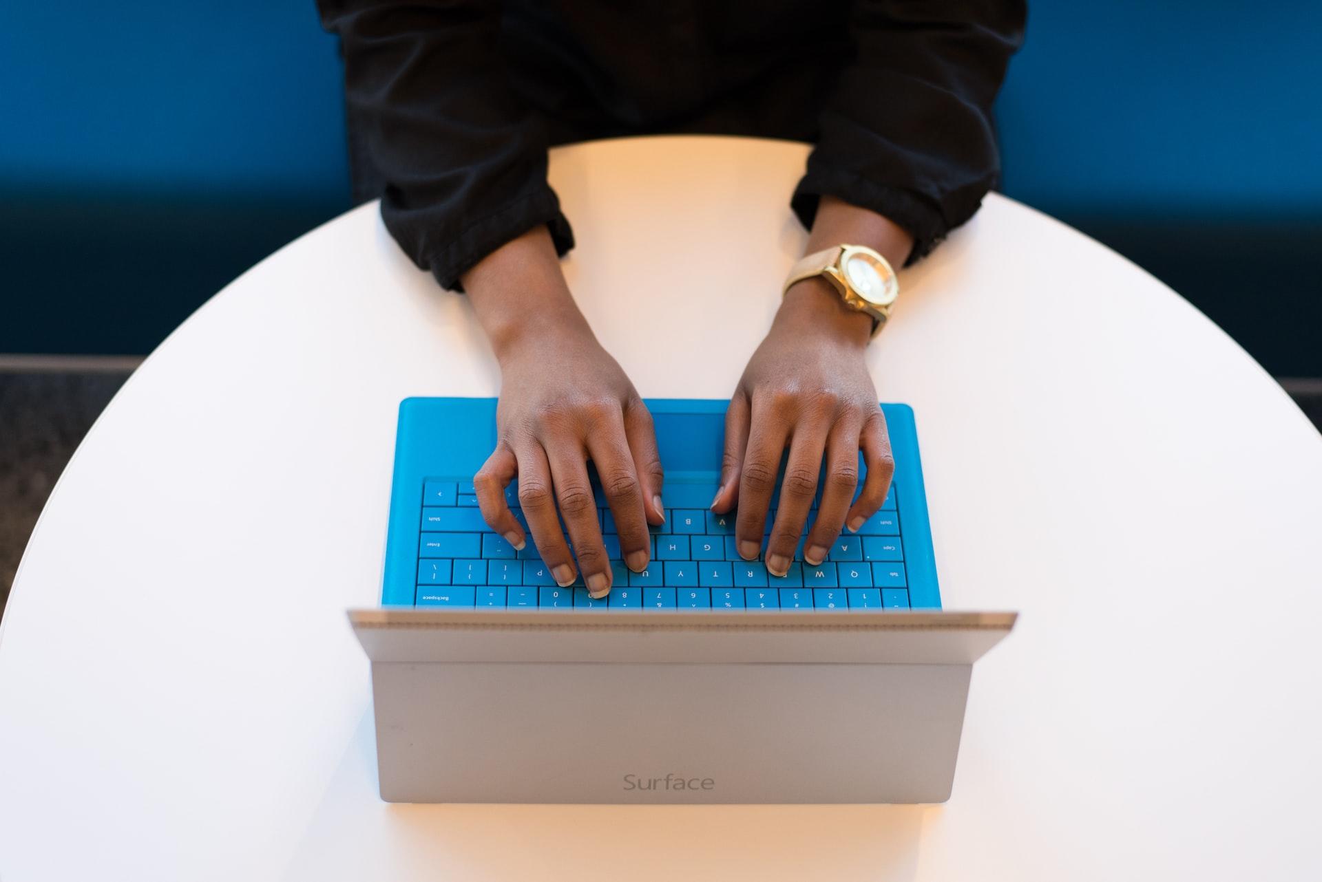 macro de mãos pousadas sobre um teclado azul em uma mesa redonda