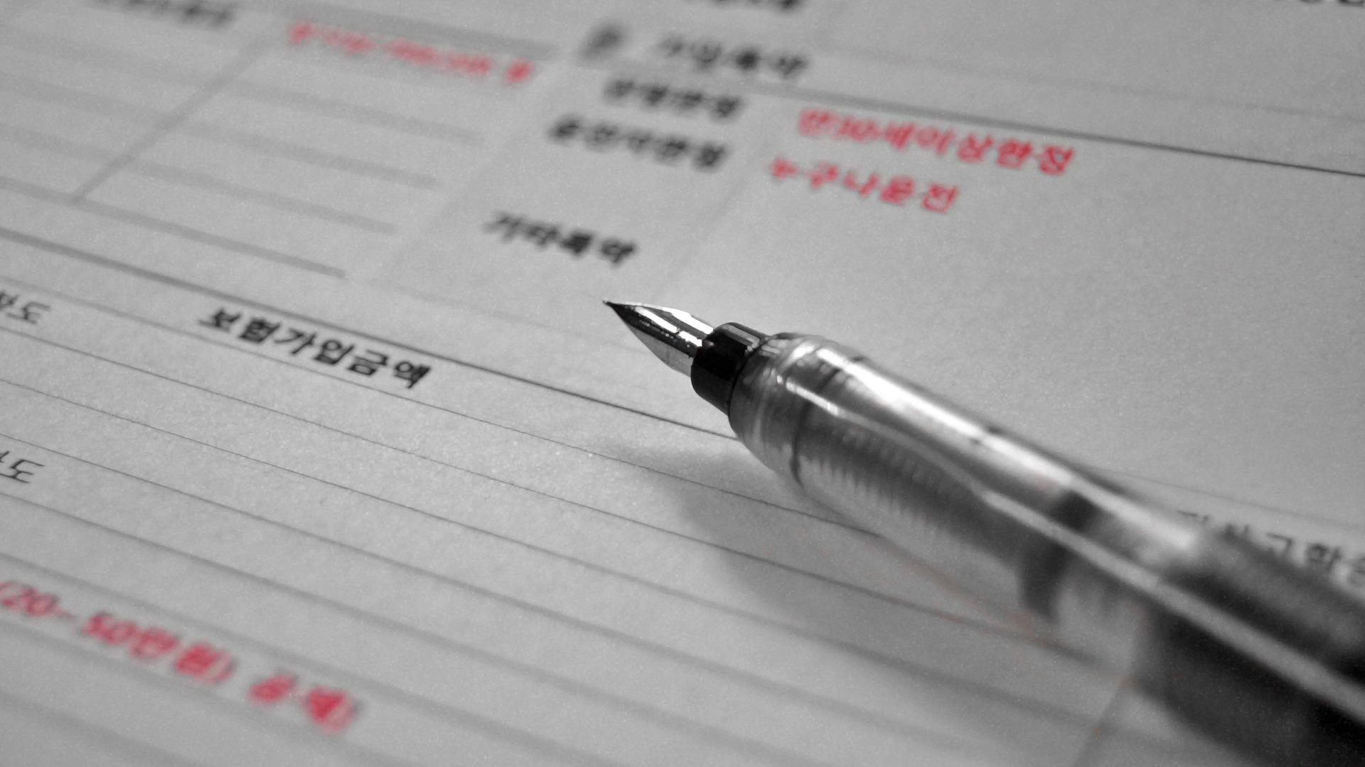 Folha pautada com caracteres coreanos impressos. Sobre a mesma, há uma caneta em destaque na imagem. 