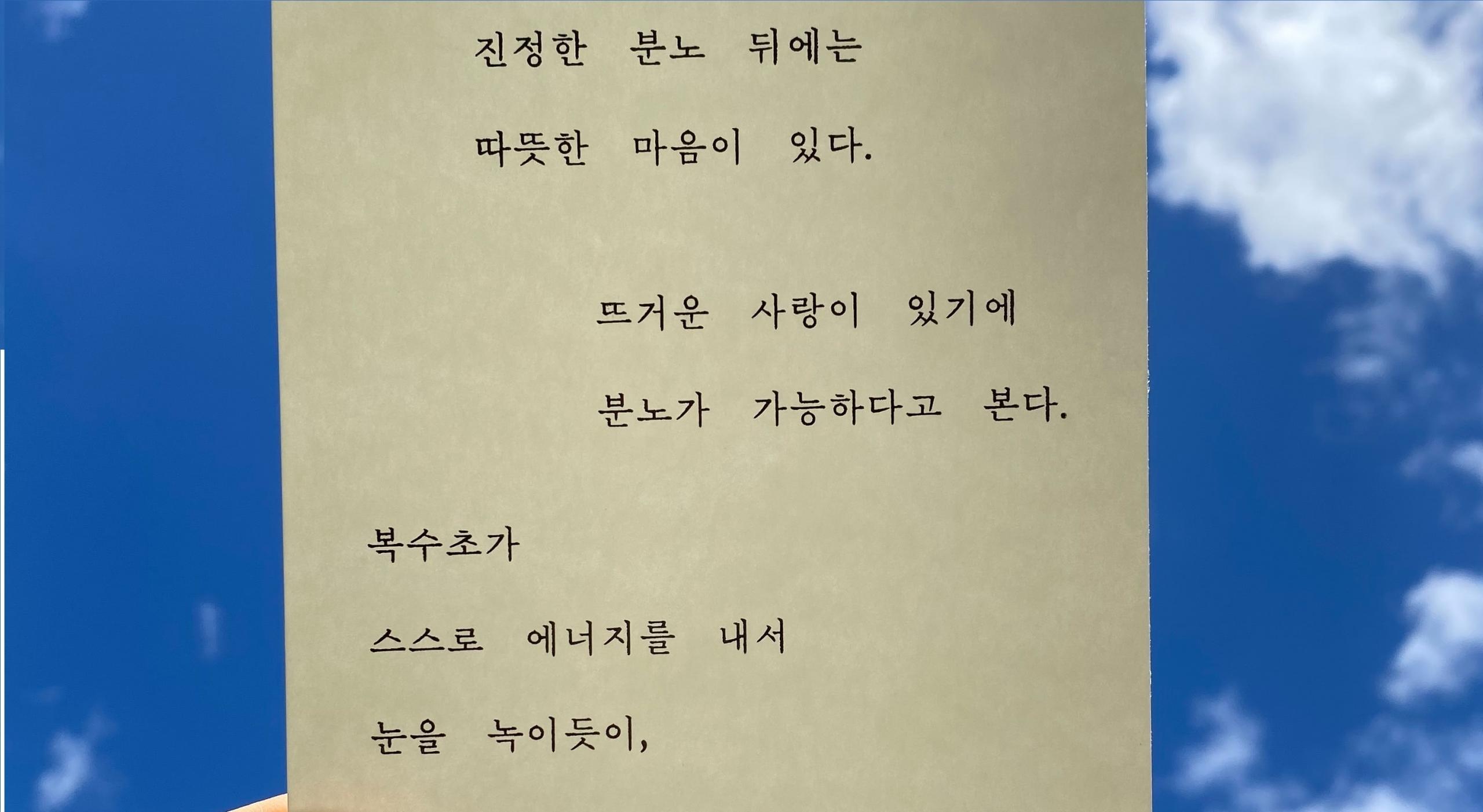 Folha branca com letras coreanas em preto no fundo azul com nuvens. 