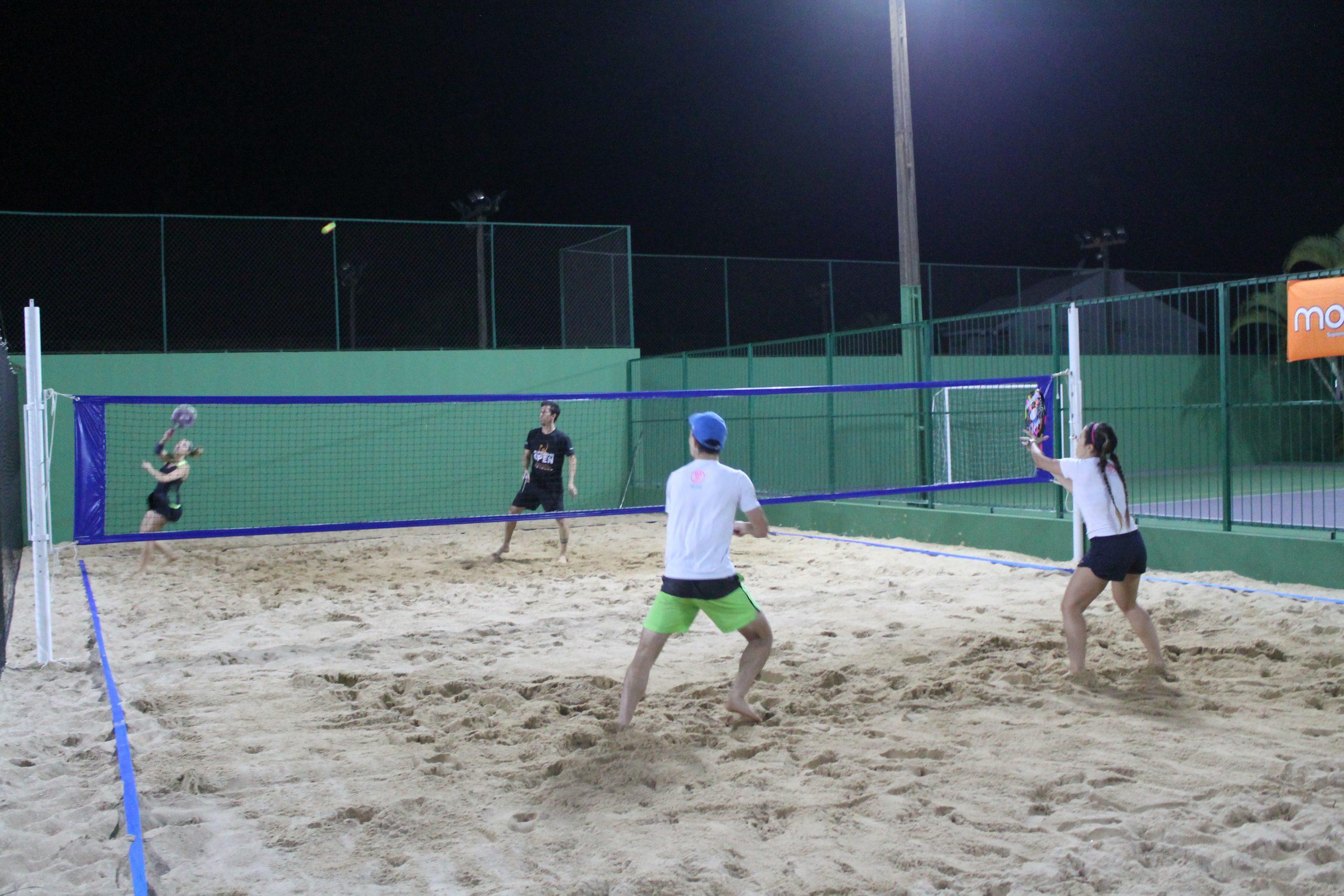 Homens jogando tênis em grupos em uma quadra de beach tennis