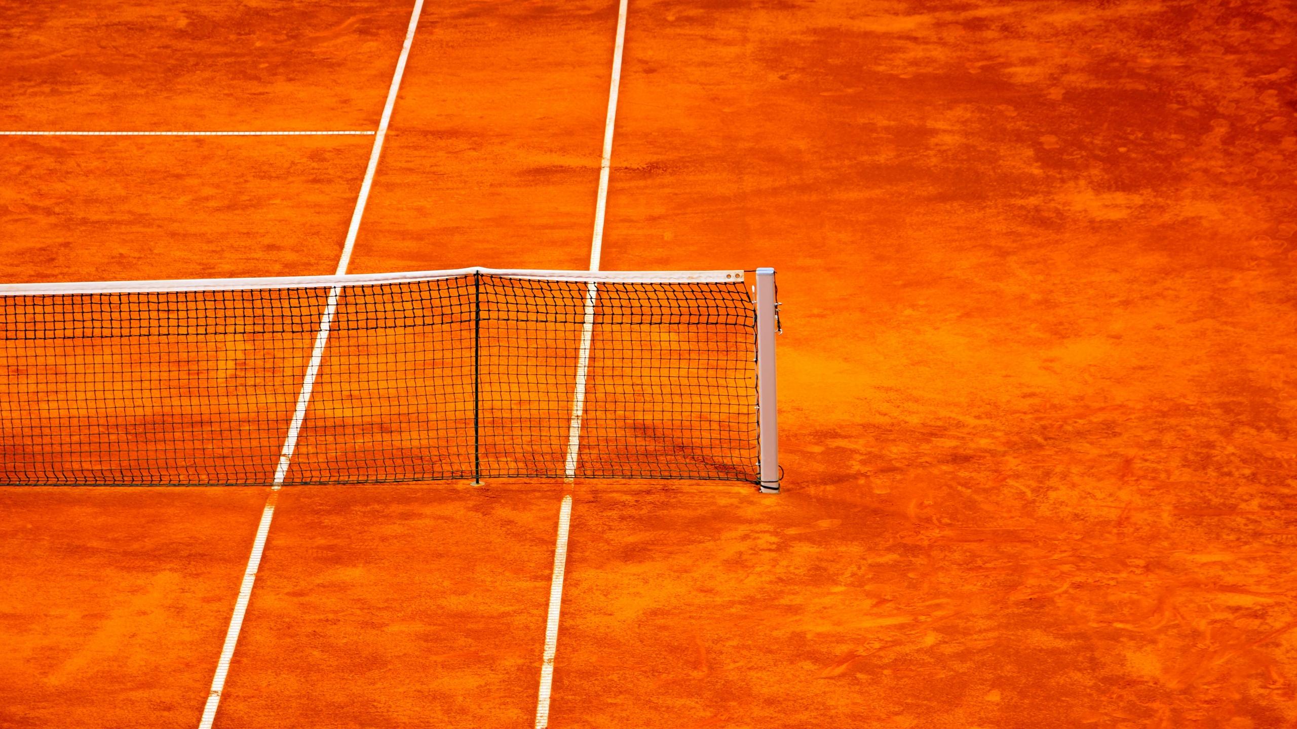 Quadra de tênis com chão delimitado na cor alaranjada e rede de tenis estendida.