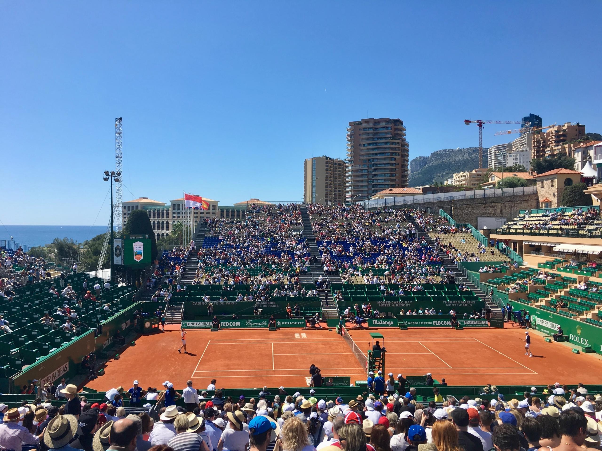 quadra ao ar livre com jogadores de tennis e o publico ocupando todos os lugares disponiveis para assistir a partida.