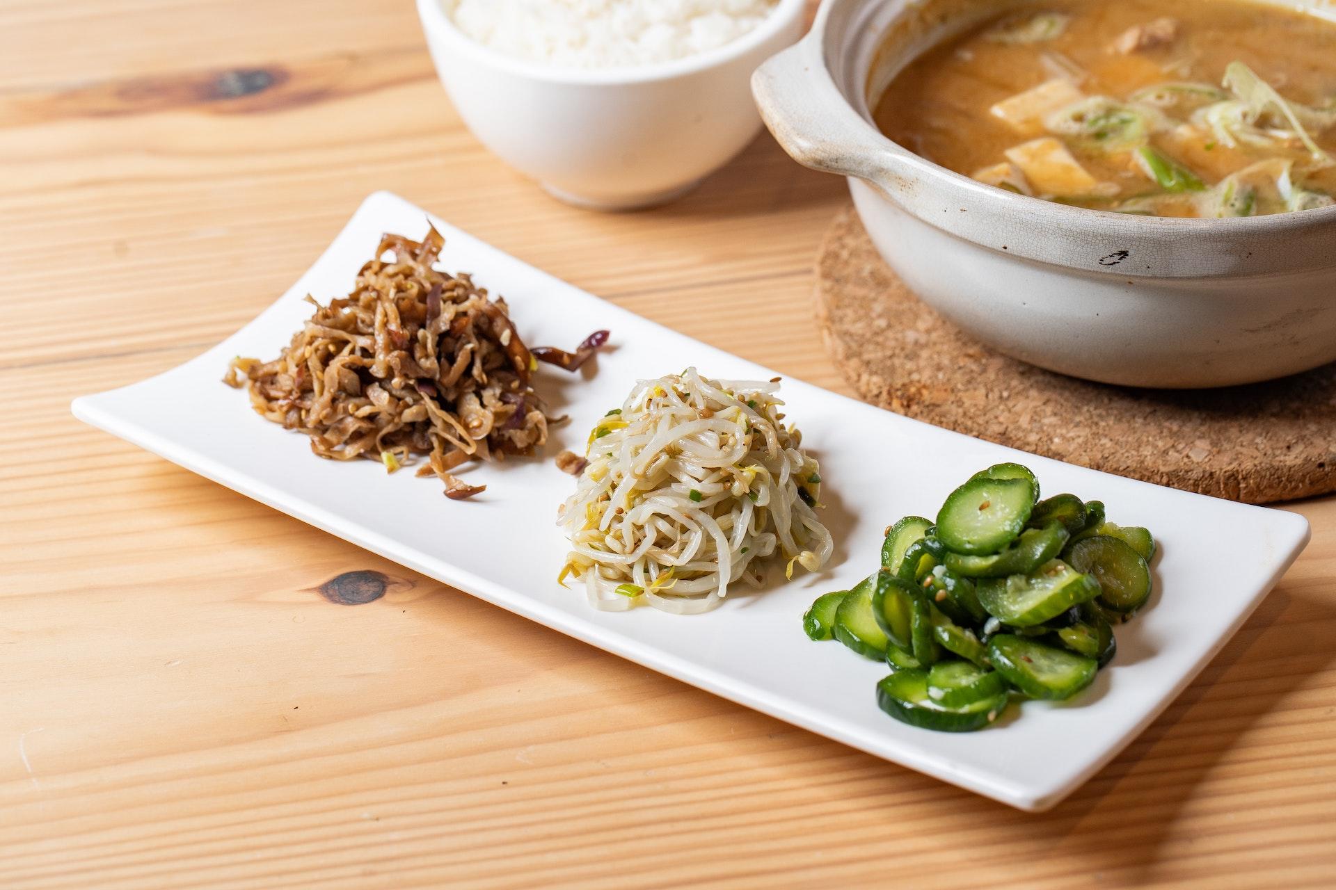 Bancada com pratos de pepinos, cogumelos e cebolas, itens para preparar o picles coreano.
