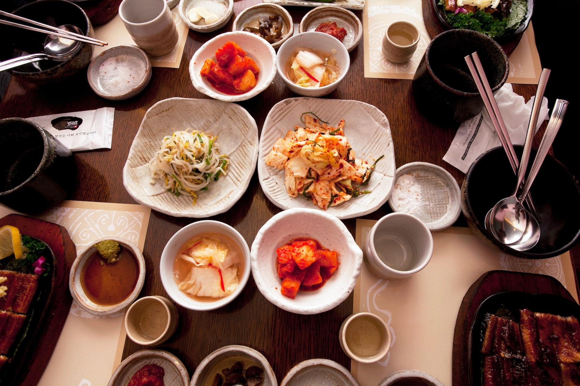 Seleção de pratos coreanos sobre uma mesa que sugere formato e iluminação de um restautante típico.