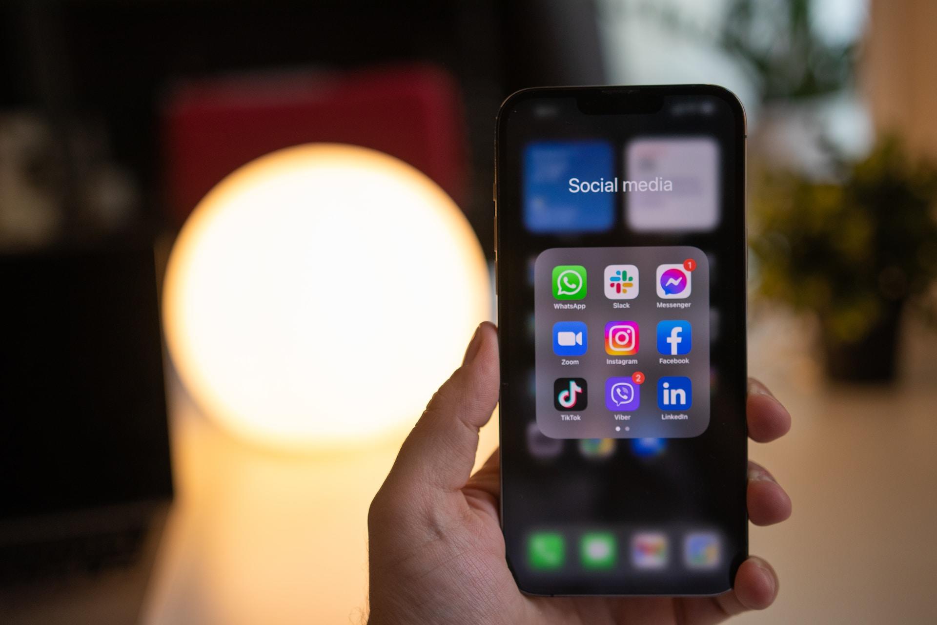 Mão segurando um celular com aplicativos de redes sociais na tela