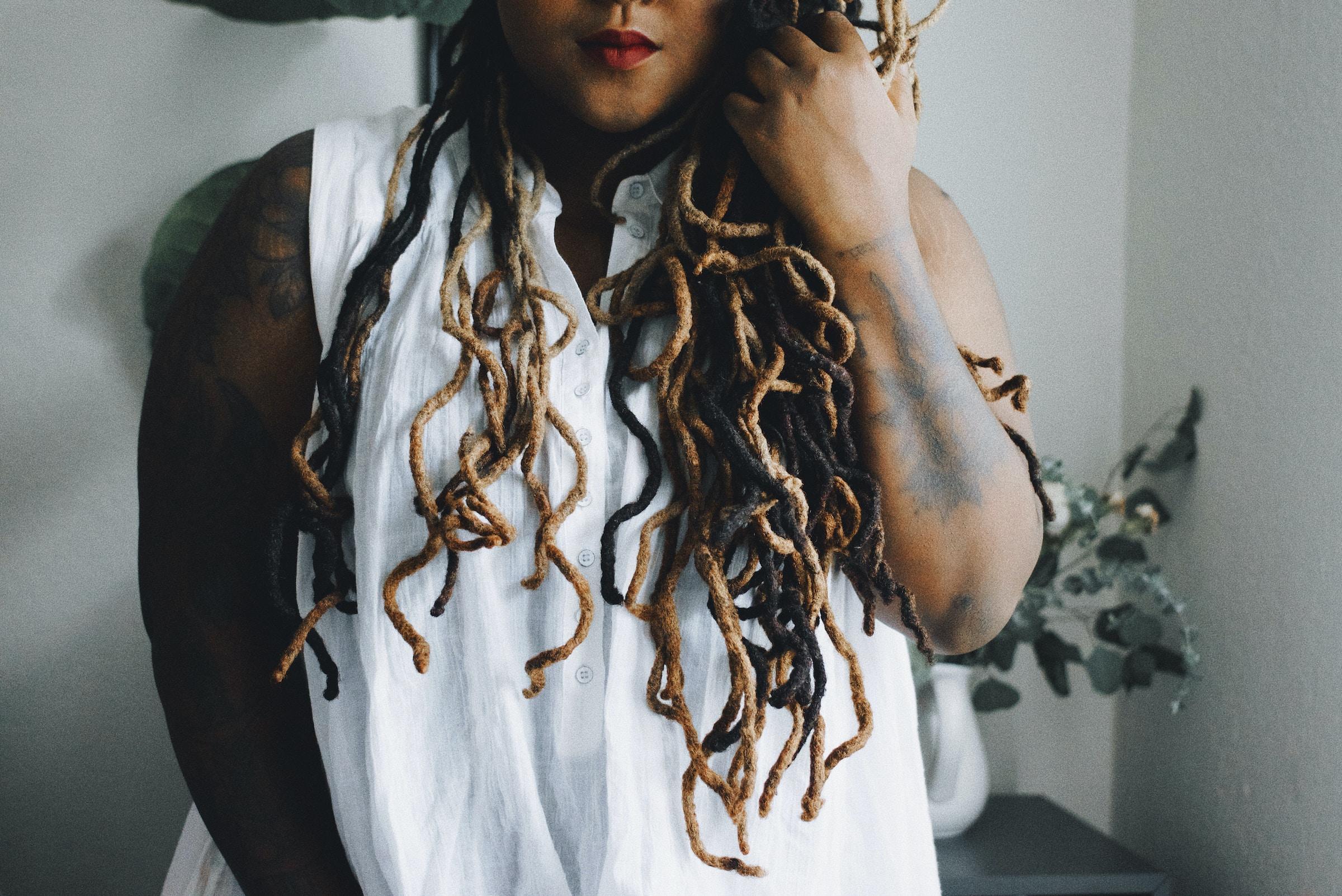 Mulher com cabelo trançado e roupa branca com tatuagem no braço