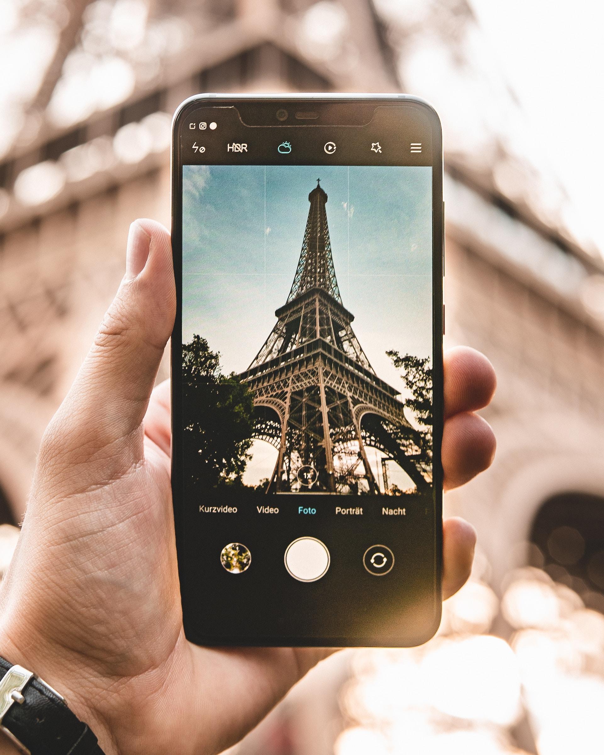 Homem fotografando a Torre Eiffel com seu celular.