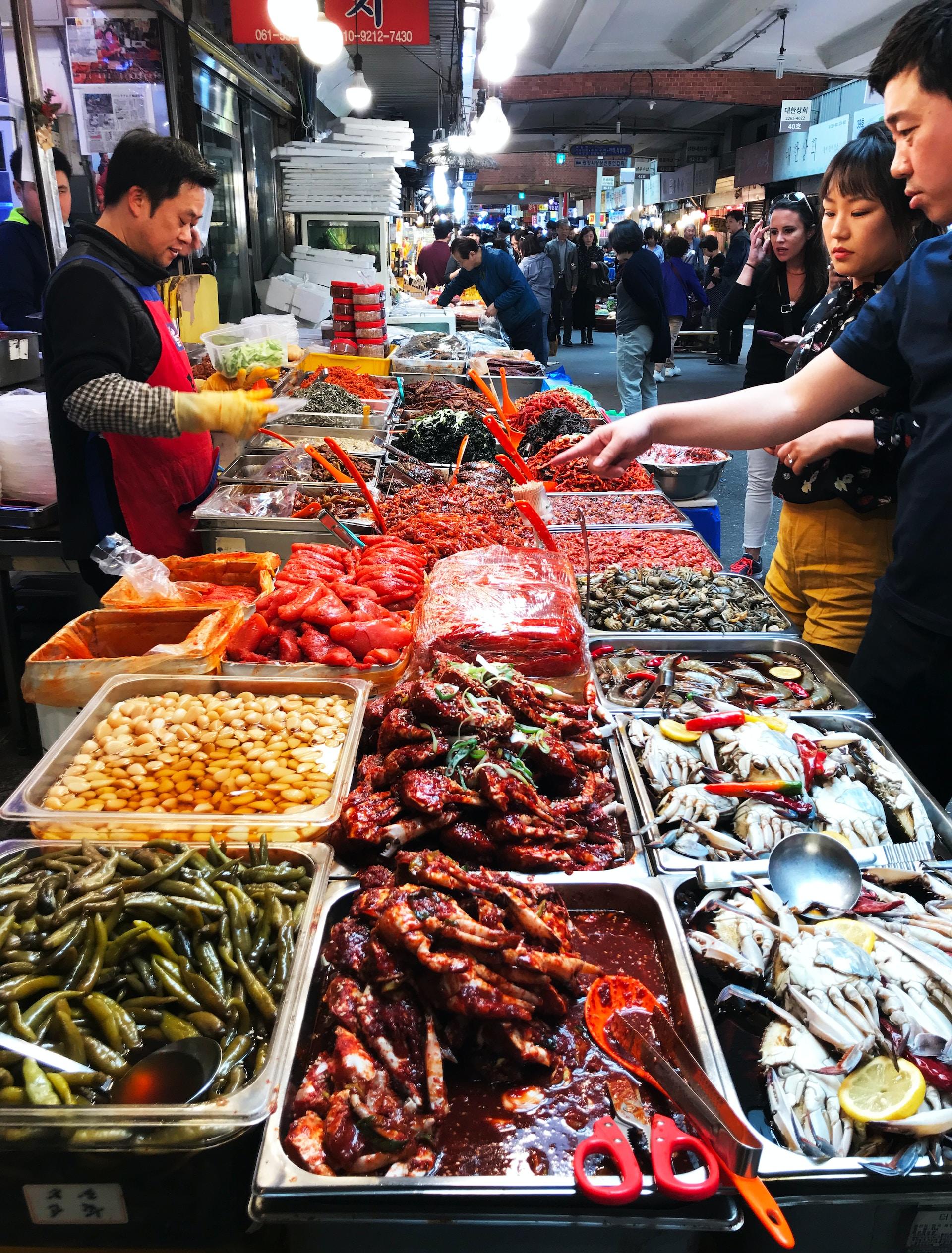 Foto de um mercado coreano com o vendedor de um lado e os clientes do outro, fazendo o seu pedido.