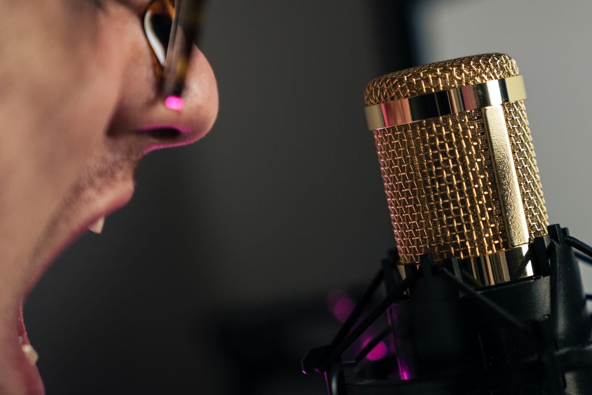 Homem de perfil cantando em um microfone dourado.
