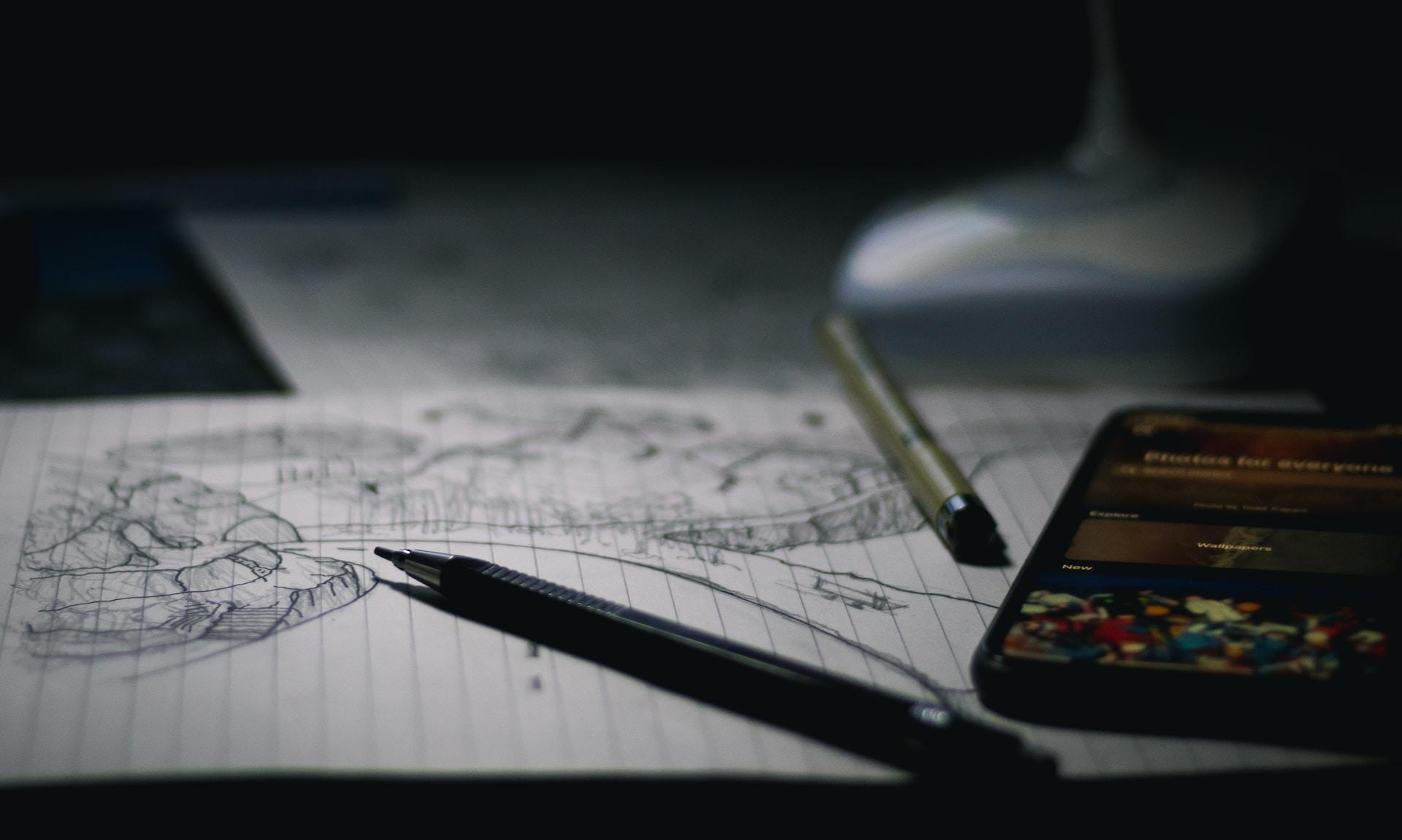folha de paleu com um desenho, uma caneta, uma lapiseira e um celular.