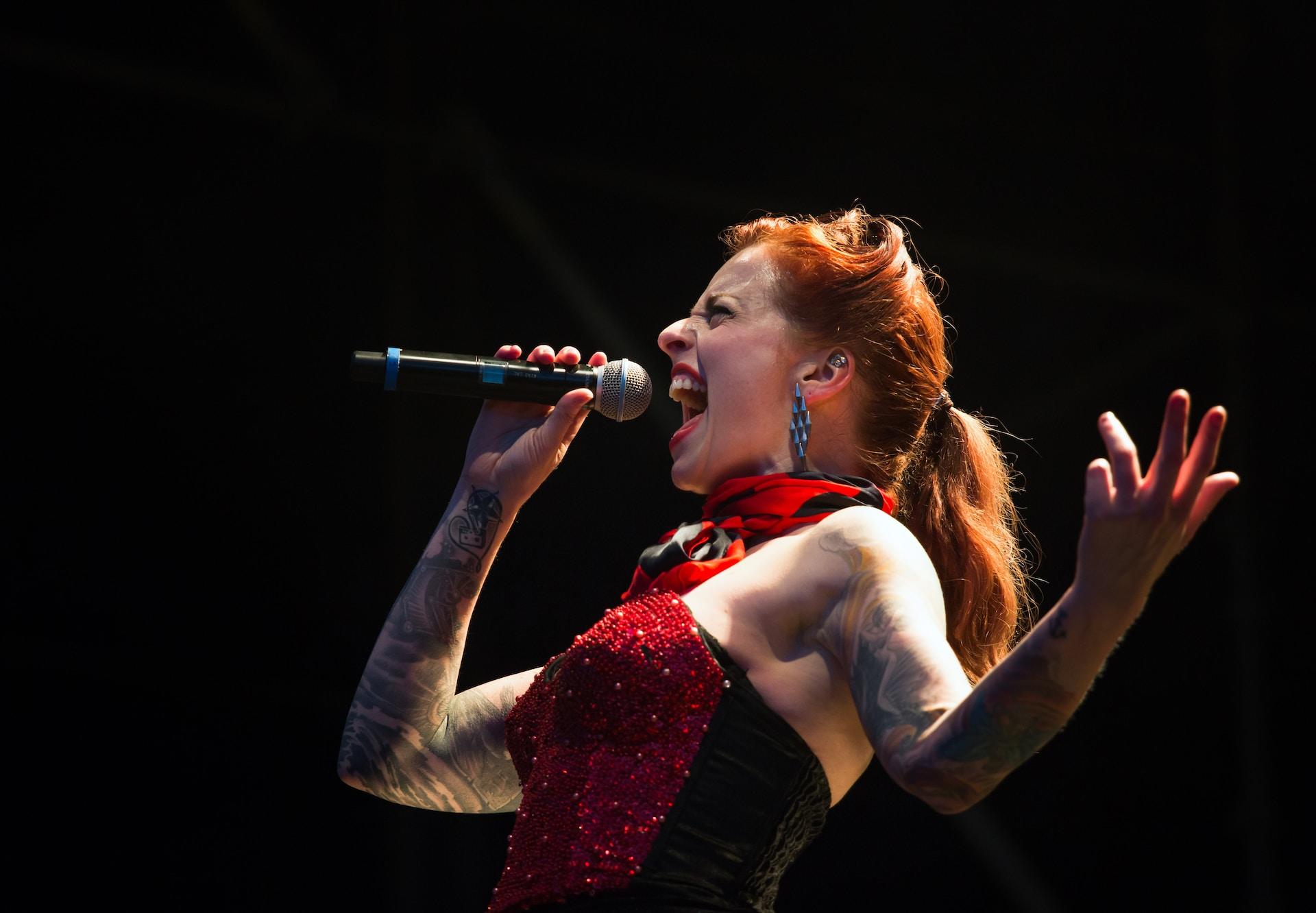 Mulher ruiva, estida de vermelho, cantando em um microfone.