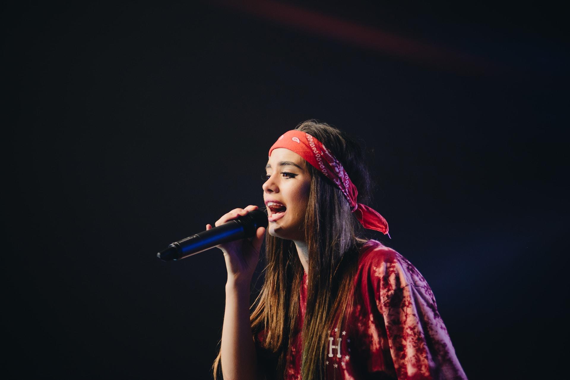 Mulher com campelos longos e uma bandana vermelha cantando em um microfone