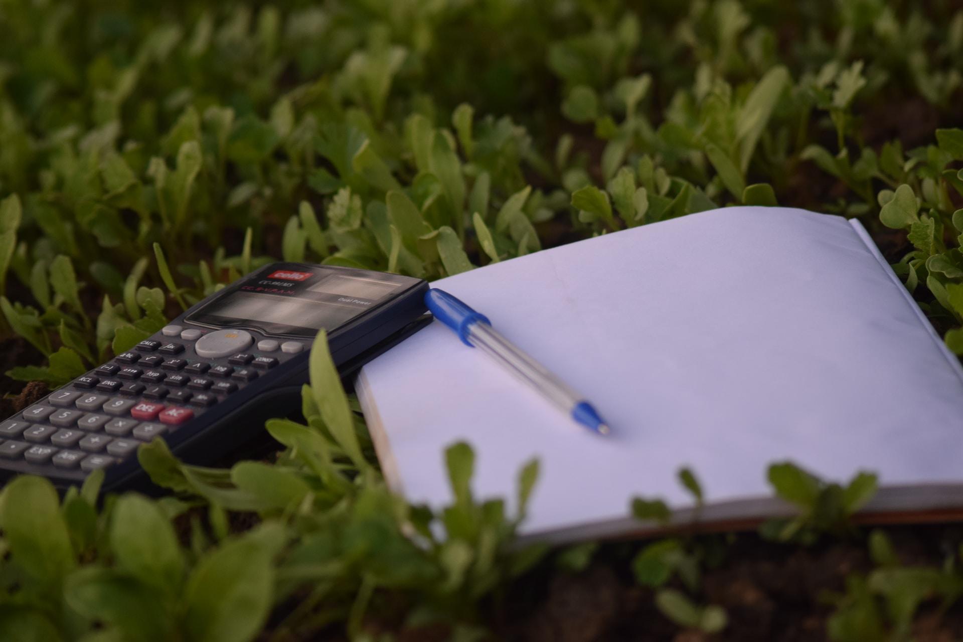 Caderno com caneta e uma calculadora em uma grama verde.