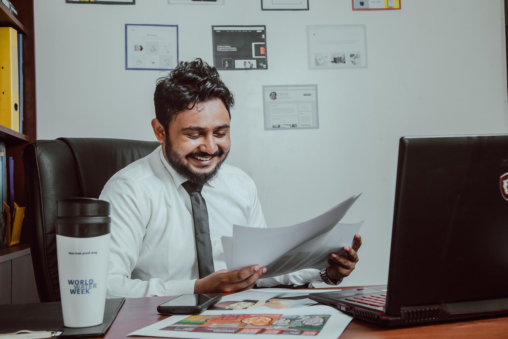 Homem em um escritório com algumas folhas na mão, sorrindo.
