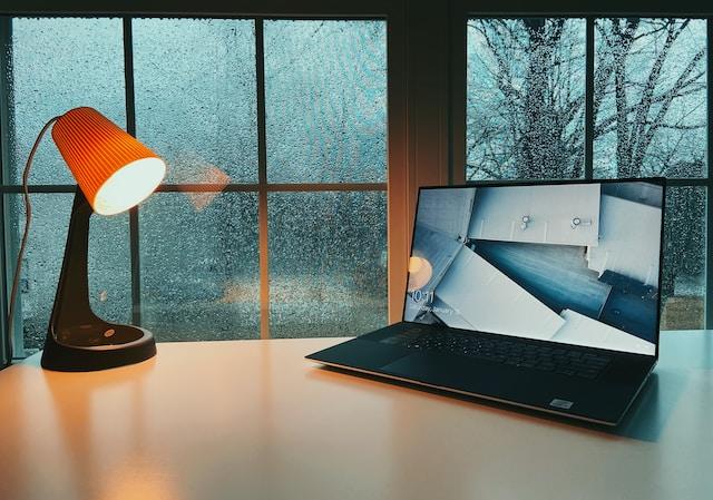 Mesa com notebook e tela arquitetônica ao lado de um abajur