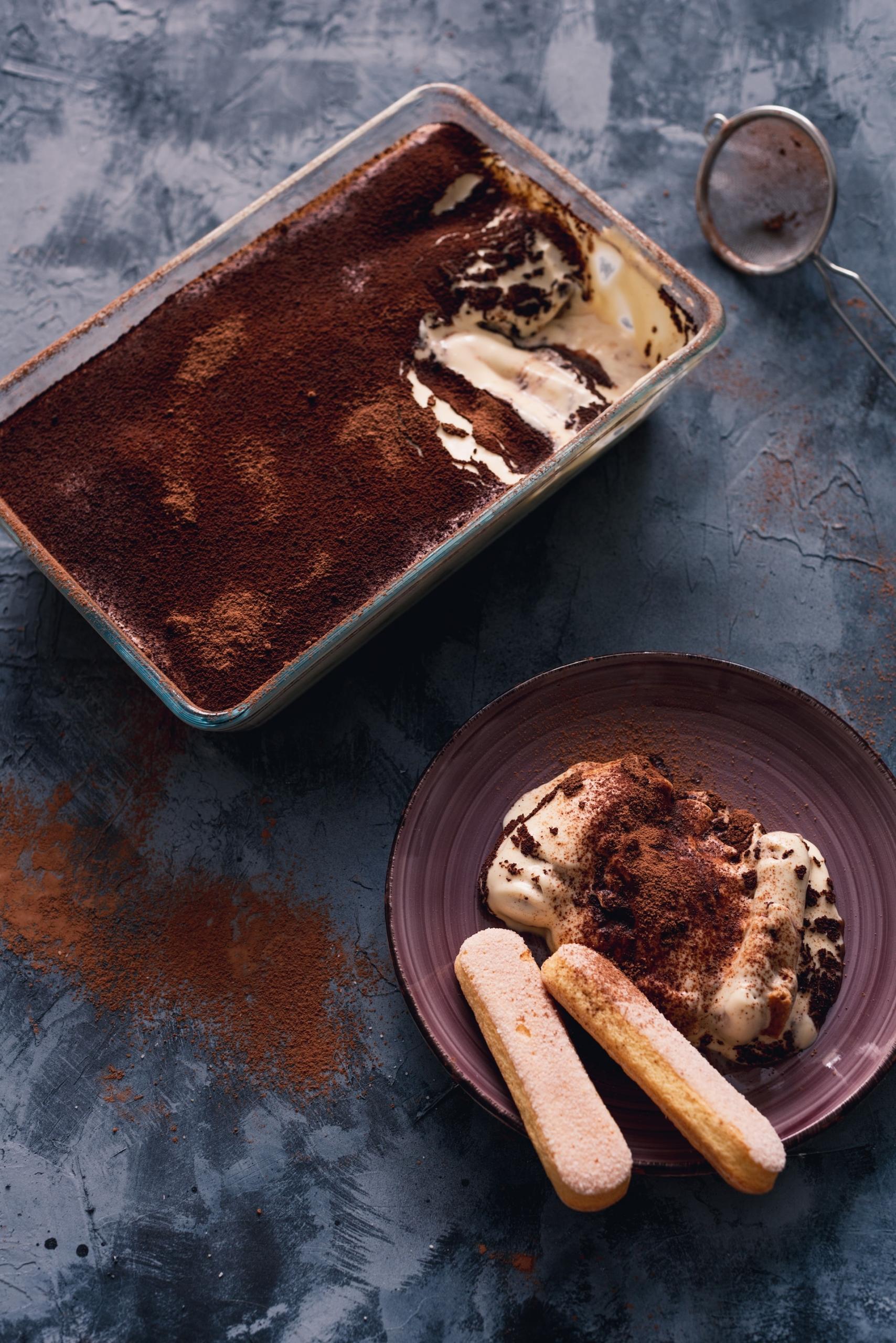 Imagem de uma travessa de vidro com tiramisu e um prato com um pedaço da sobremesa