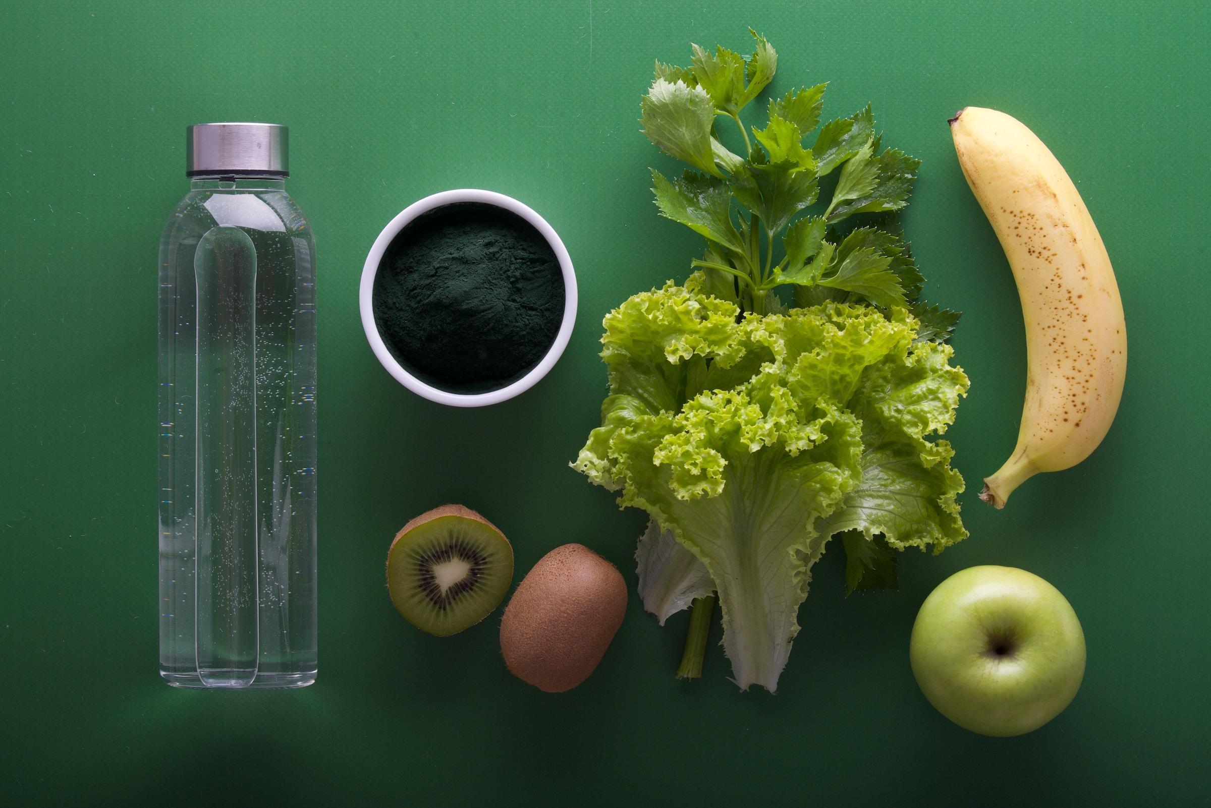 Uma banana, uma maça, um kiwi, saladas e uma garrafa com água.