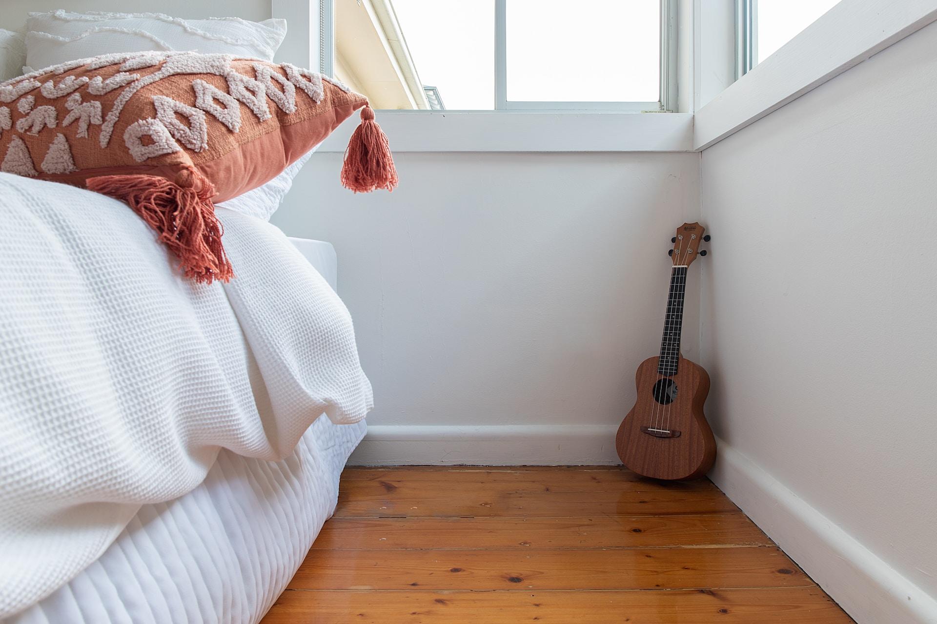 Foto de um quarto com uma cama e um cavaquinho ao fundo.