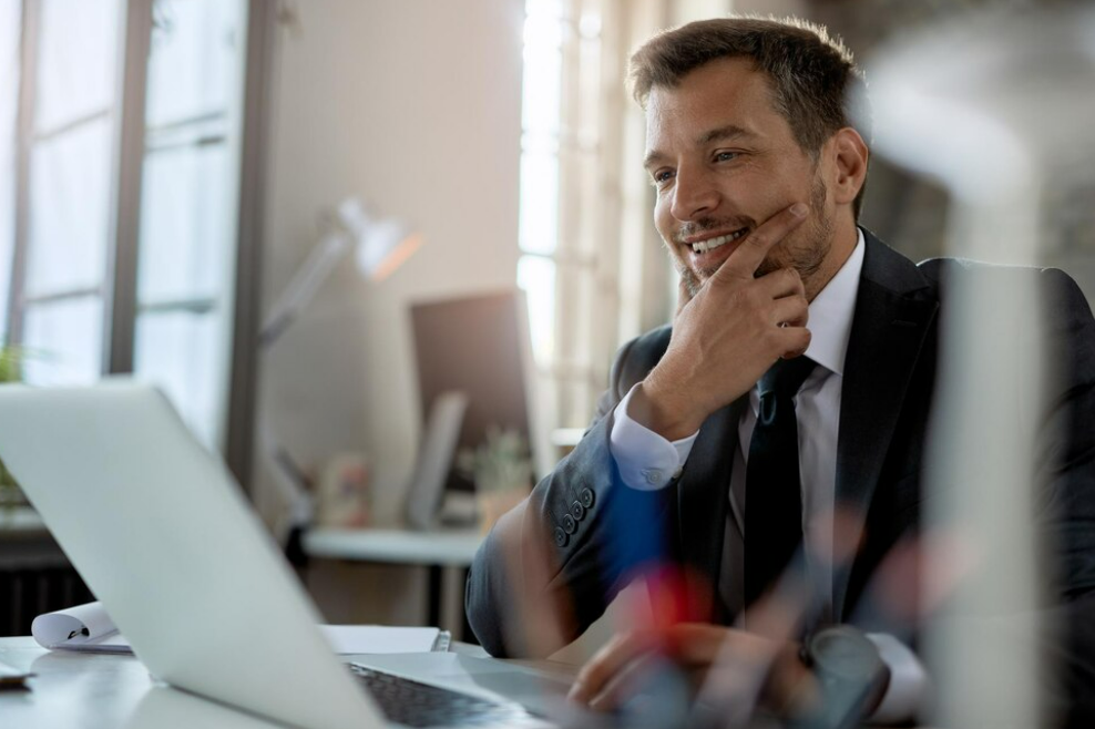Imagem de homem investindo enquanto sorri em frente a um computador