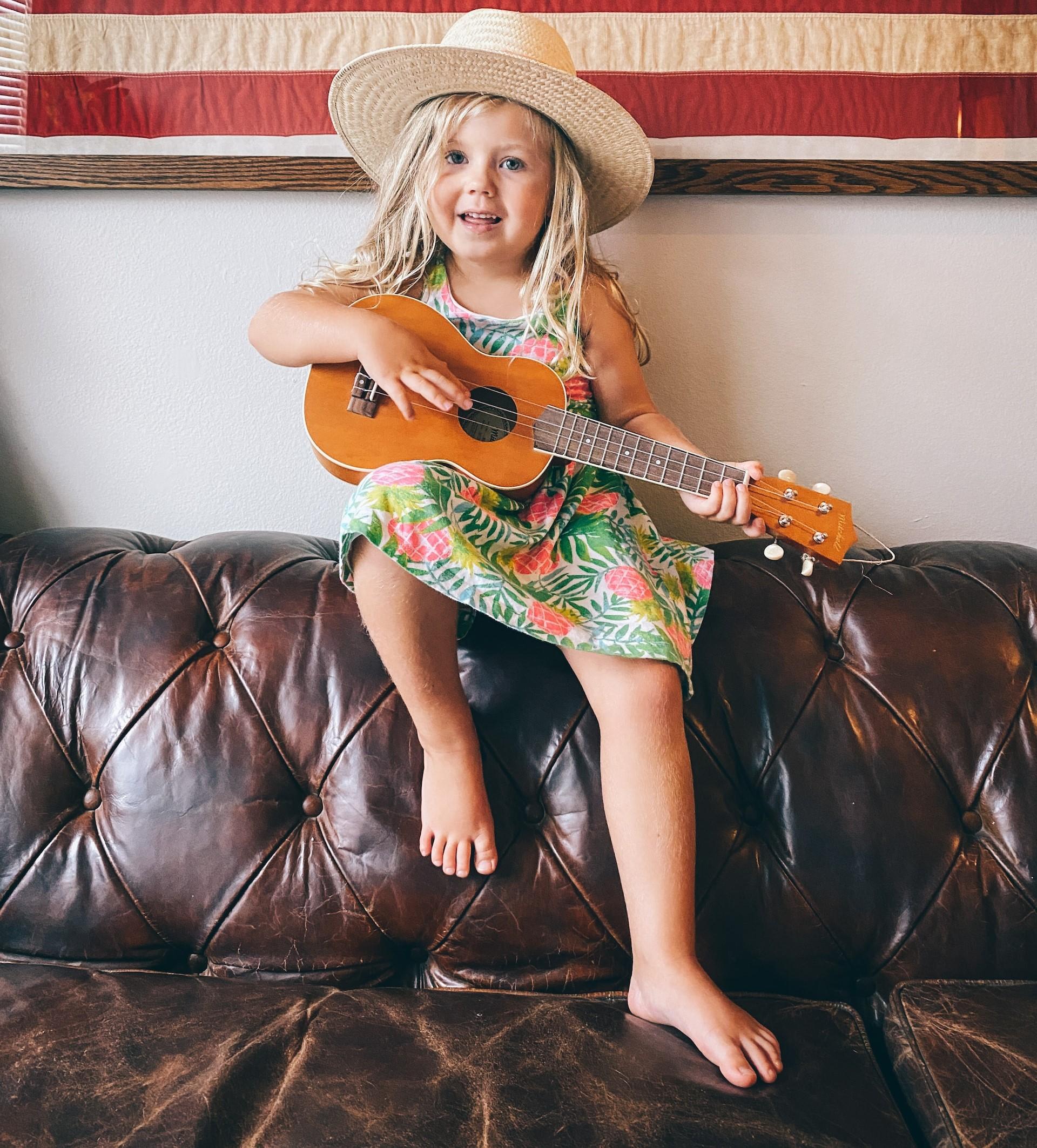Menina loira em um sofá de couro tocando cavaquinho.