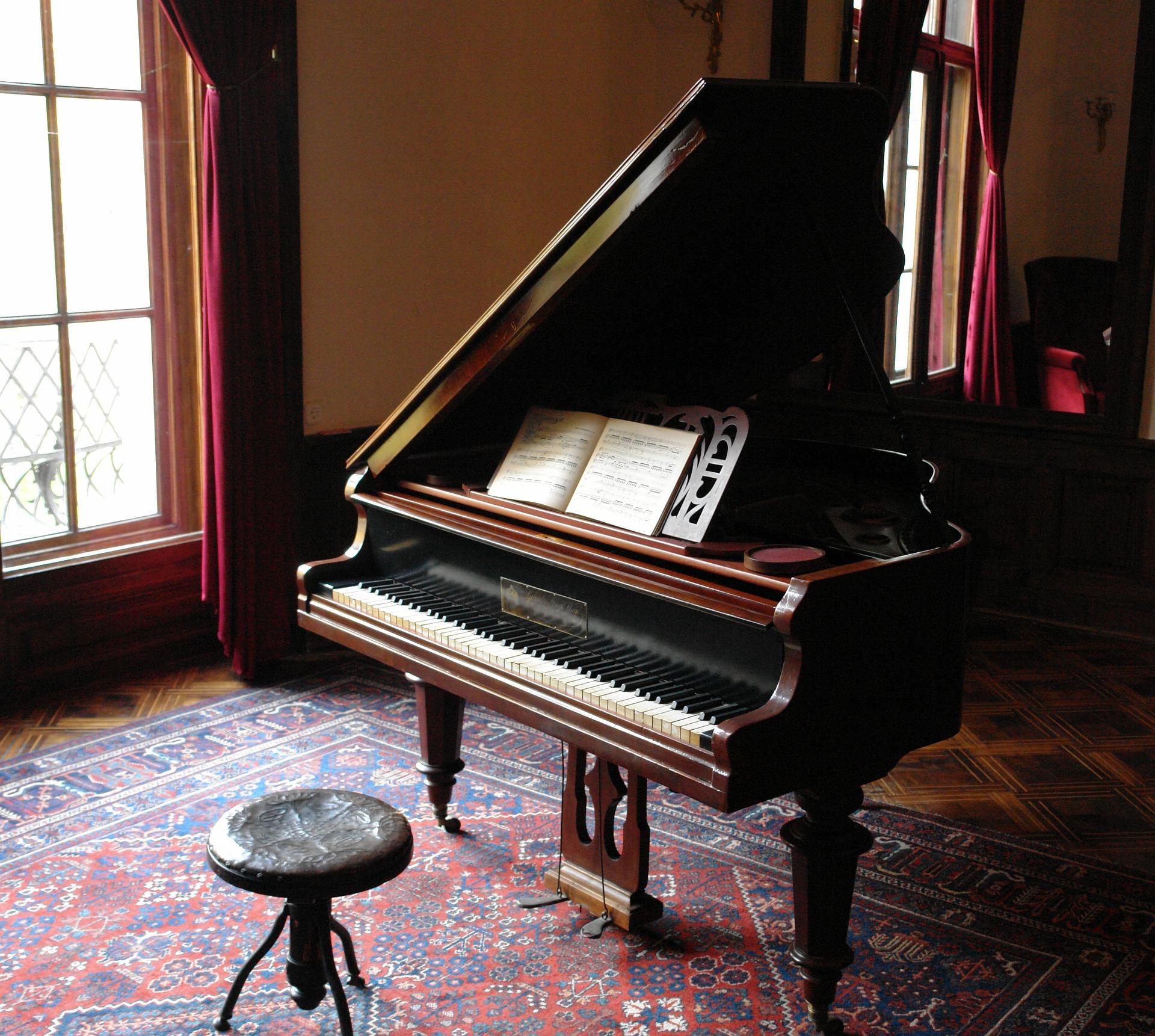 Piano de calda em uma sala com tapete e cortinas em tom de vinho.