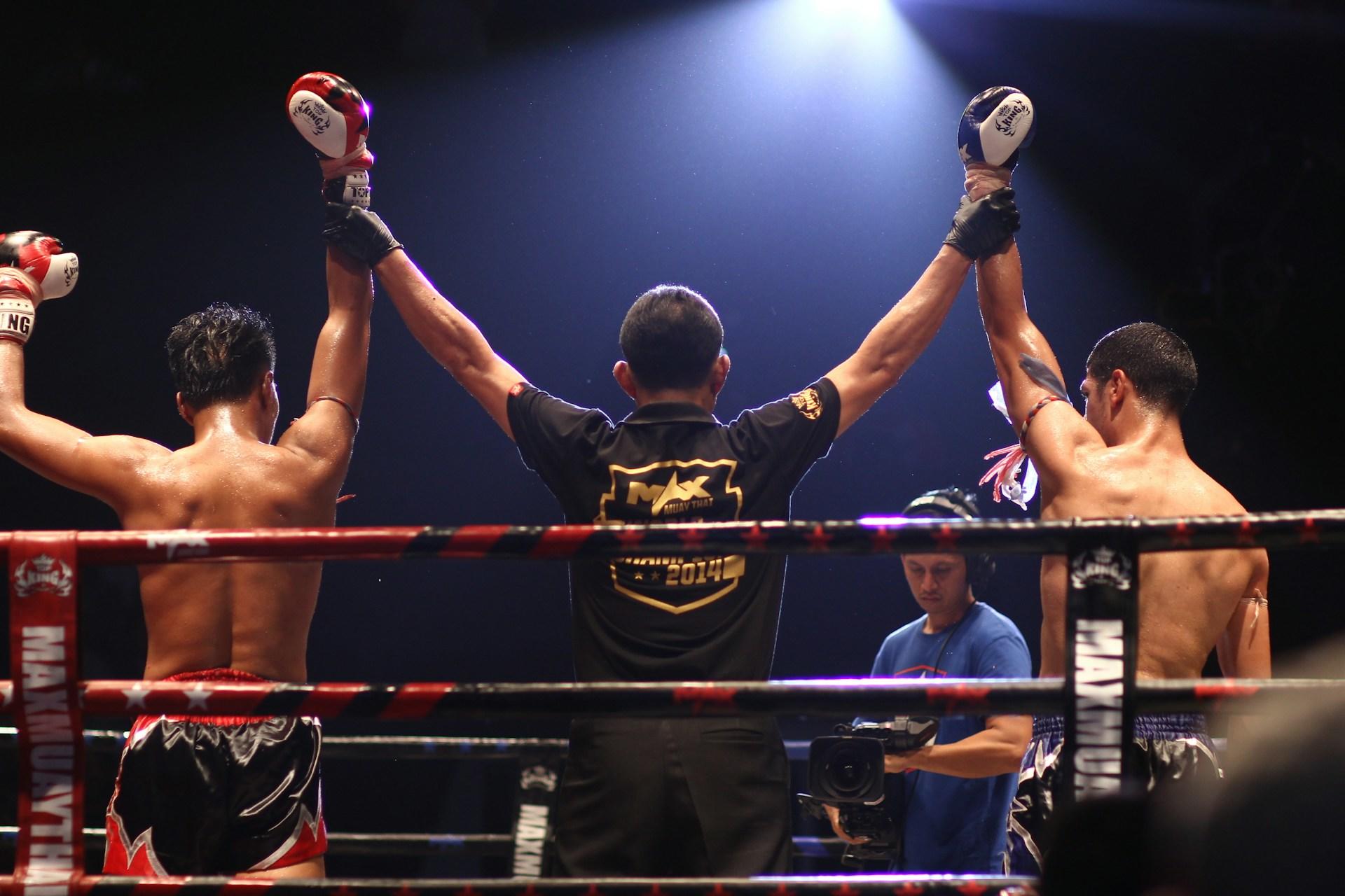 Foto do juiz levantando as mãos dos lutadores de boxe no ringue.
