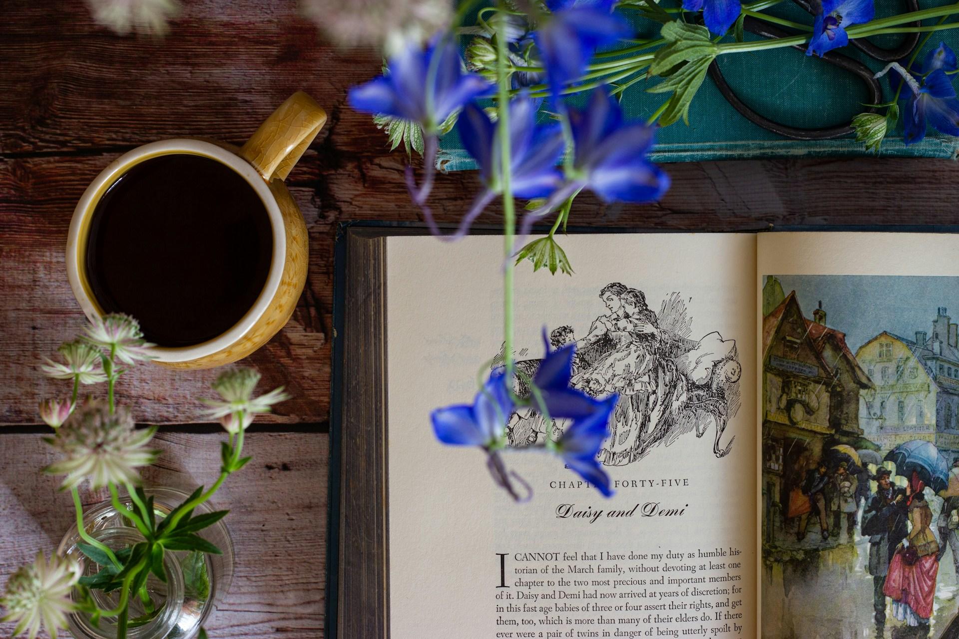 Fotografia de obra de Dante ao lado de copo com café e flores