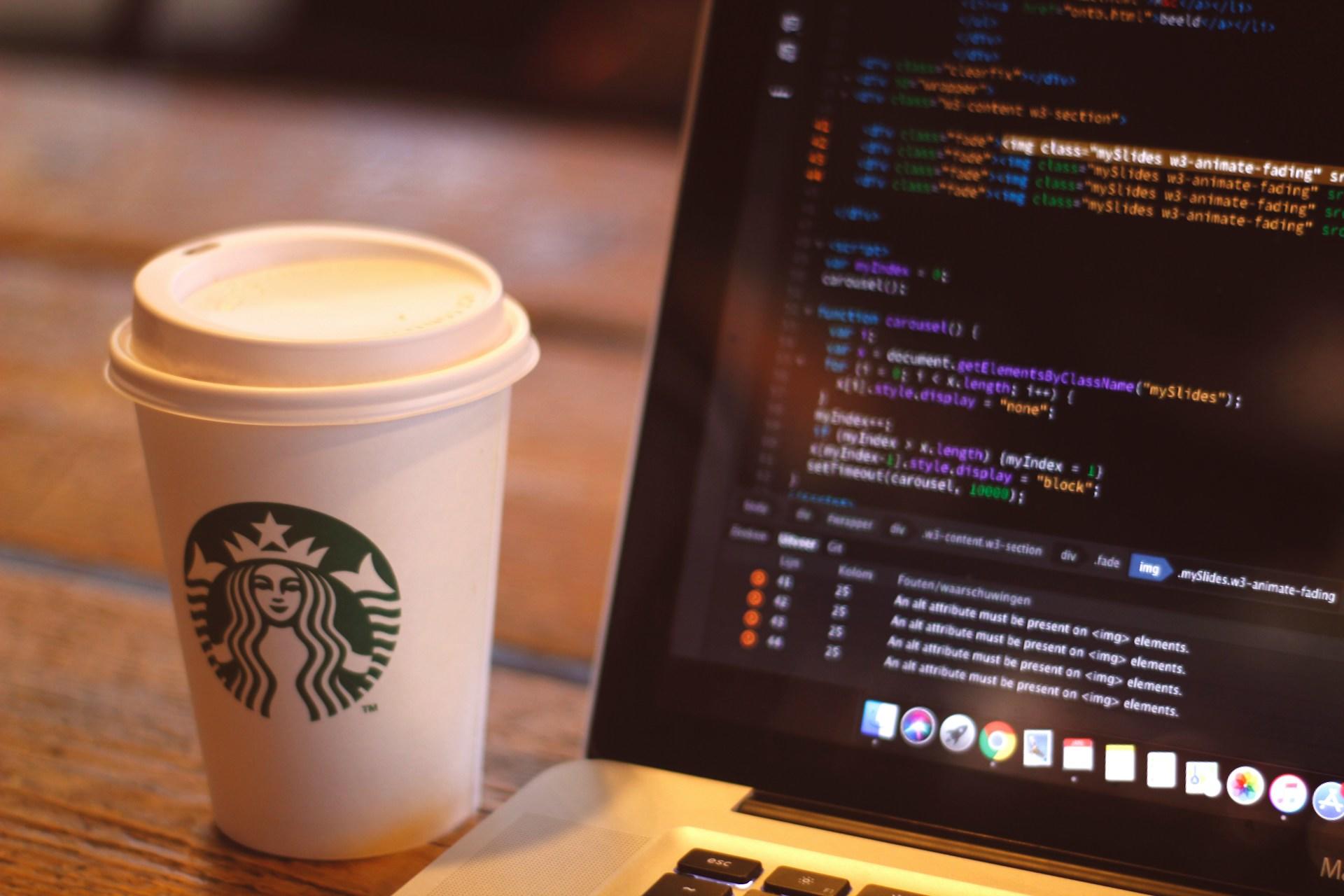 Fotografia de copo de café ao lado de tela com código de programação