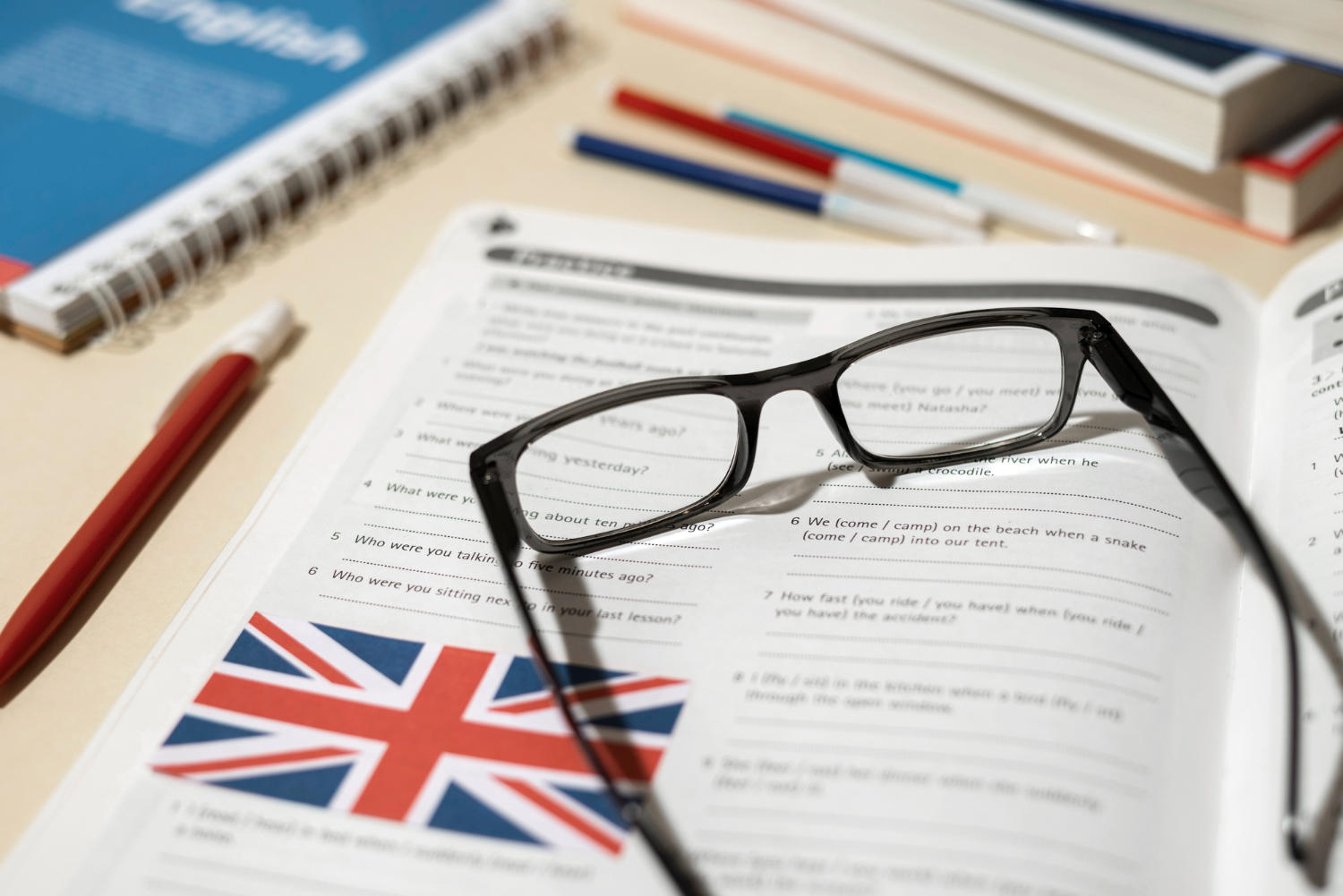 Livro com questões de inglês, óculos e lapiseira em cima da mesa.