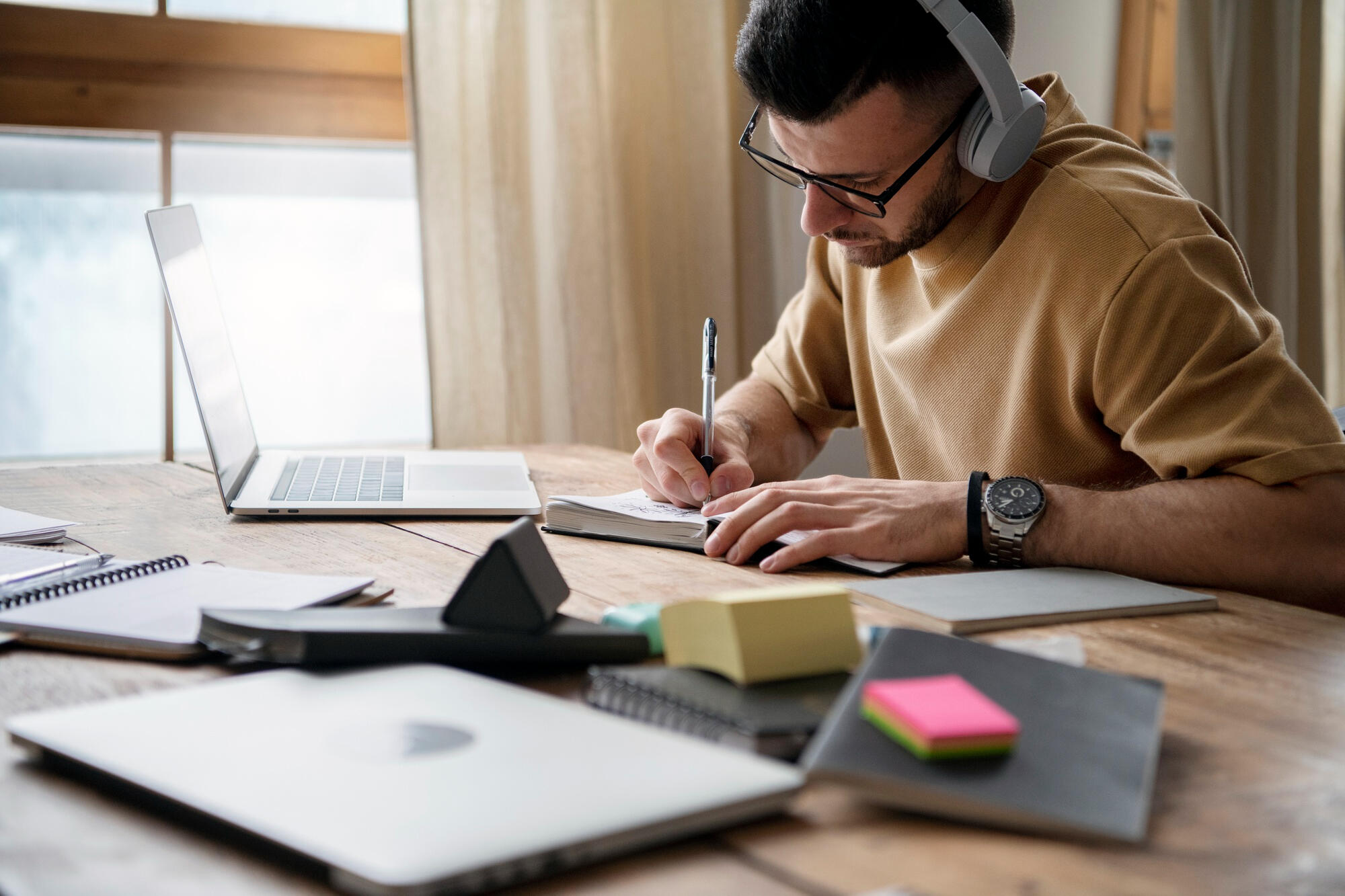 Homem estudando, com fone de ouvido, notebook e escrevendo em um caderno!