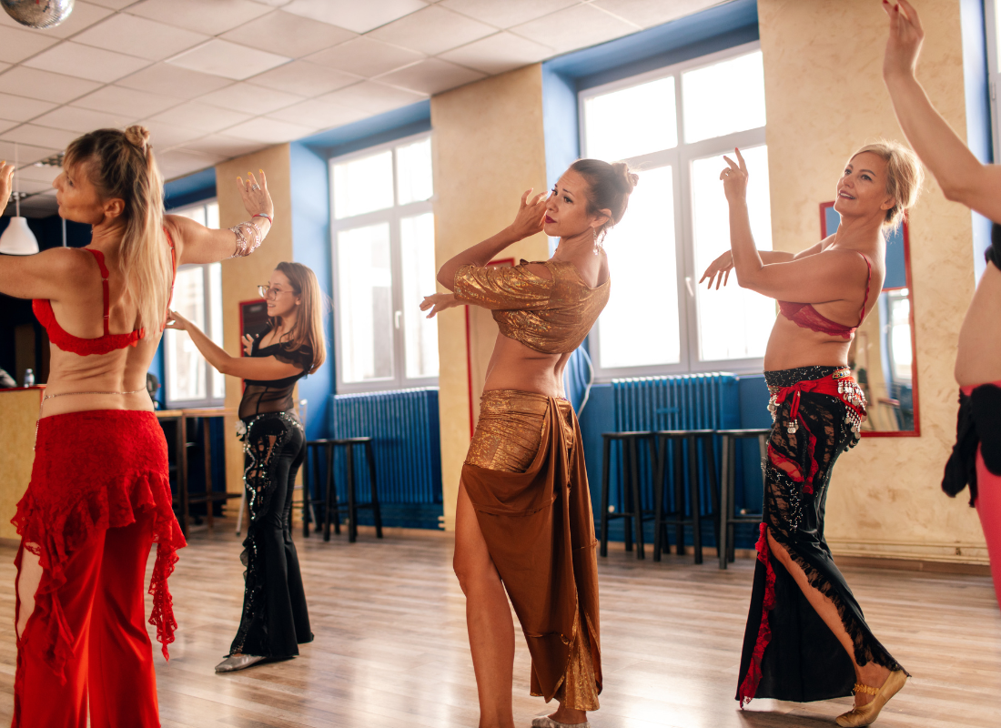 Salão com várias mulheres com trajes de dança oriental aprendando a dançar