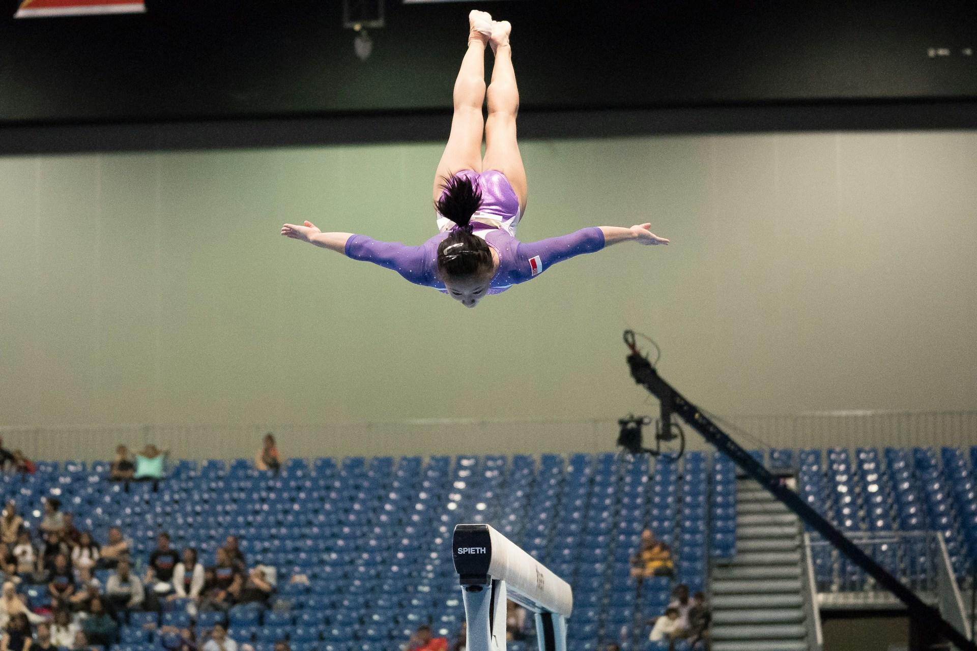 Mulher fazendo um salto sobre uma trave de equilíbrio