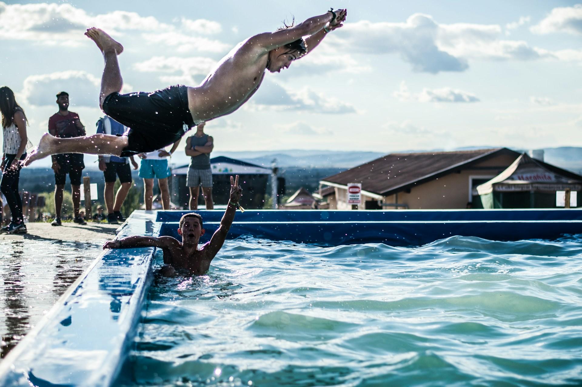Pessoa pulando em piscina com outras no fundo