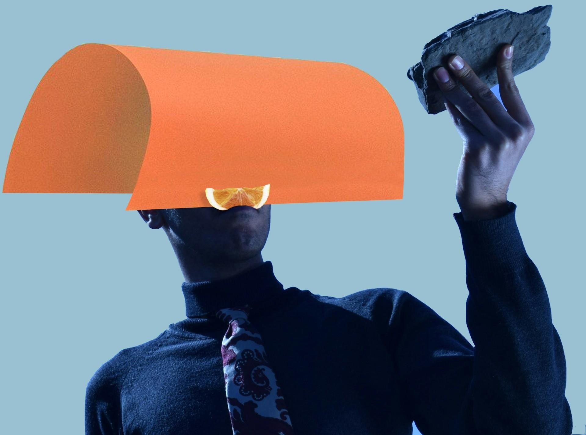 Foto abstrata de uma pessoa com um papel laranja na cabeça observando uma pedra na mão.