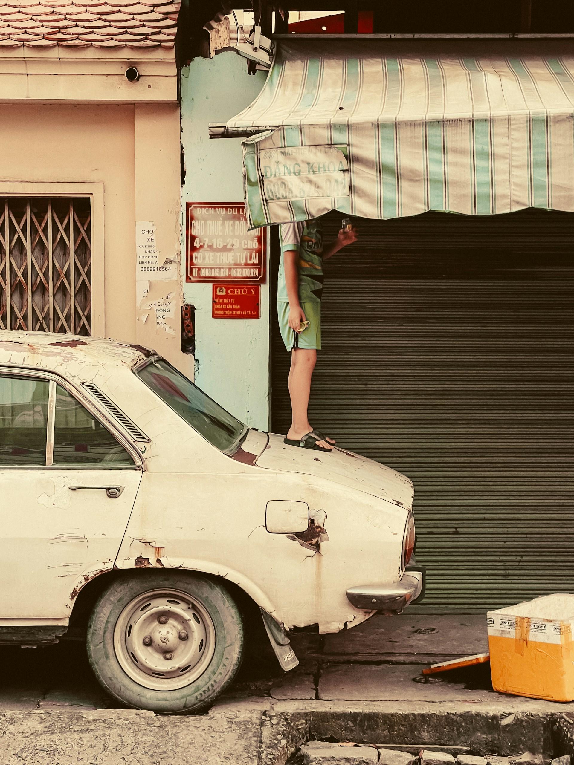 Foto de uma criança em cima de um carro velho.