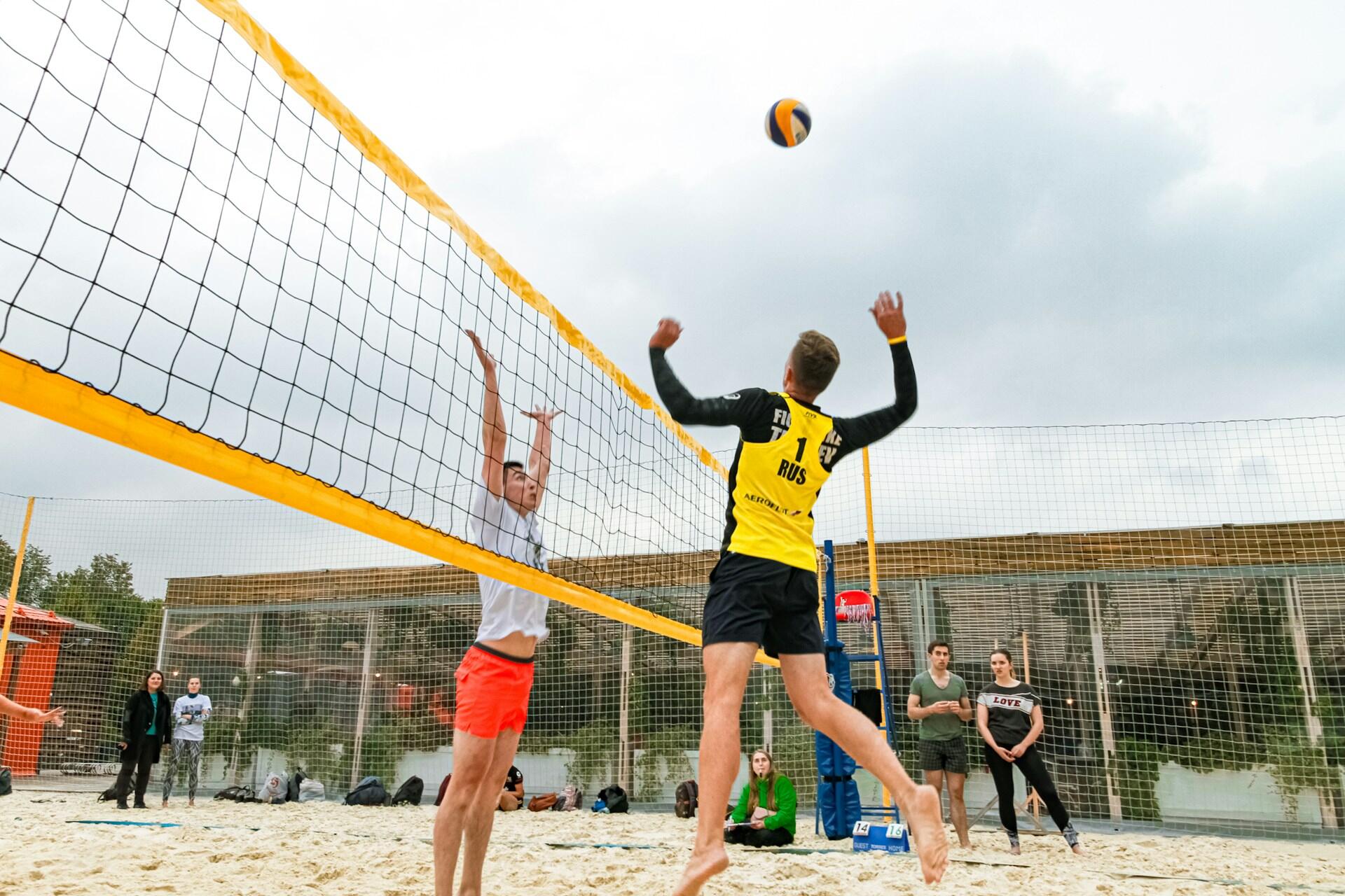 Dois homens saltando em uma rede de volei de praia, um para atacar e outro para defender