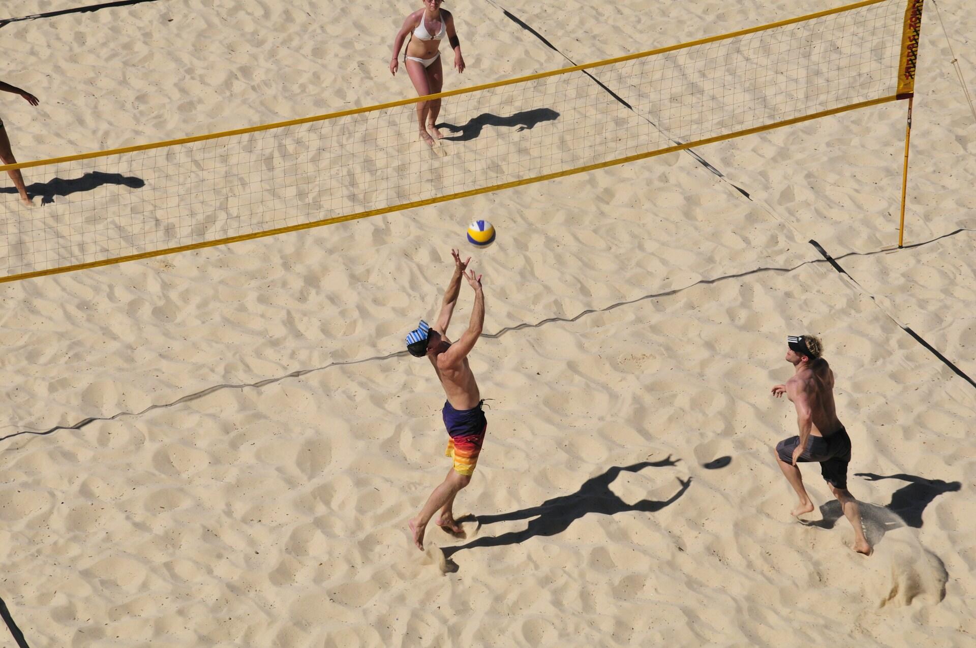 Dupla masculina jogando volei de praia contra uma dupla feminina.